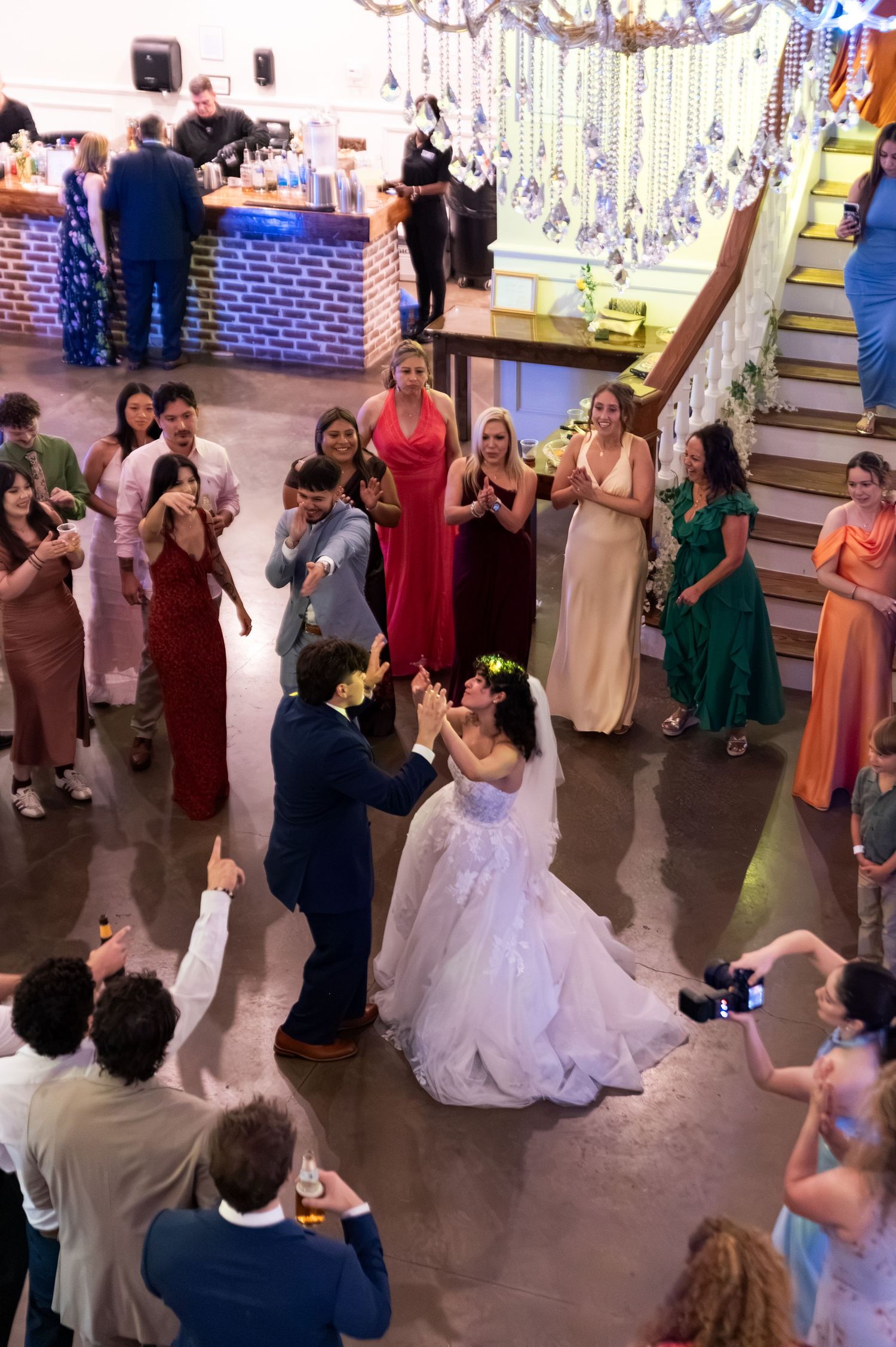 Bride and groom celebrate joyful first dance surrounded by cheering guests at wedding reception.