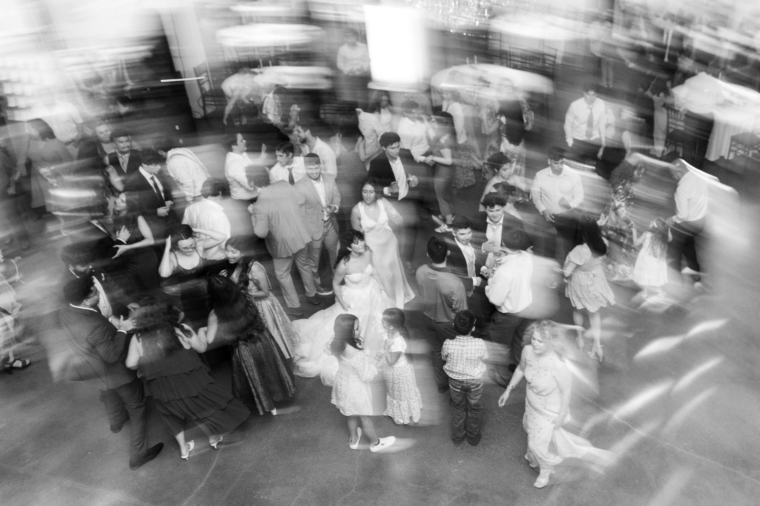 Black and white motion-blur photo of guests dancing energetically at a wedding reception.