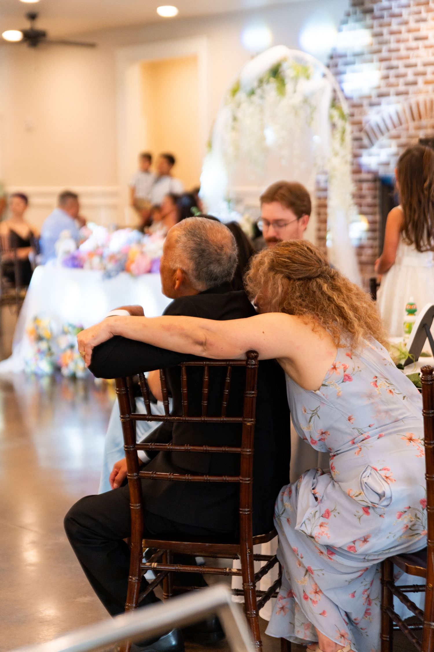 Wedding guests seated at reception table sharing an affectionate moment during the celebration.