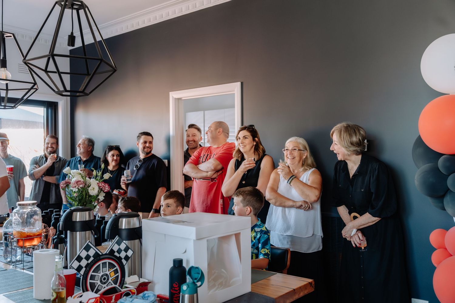 Party guests mingling in modern room decorated with orange and black balloons and geometric light fixtures.