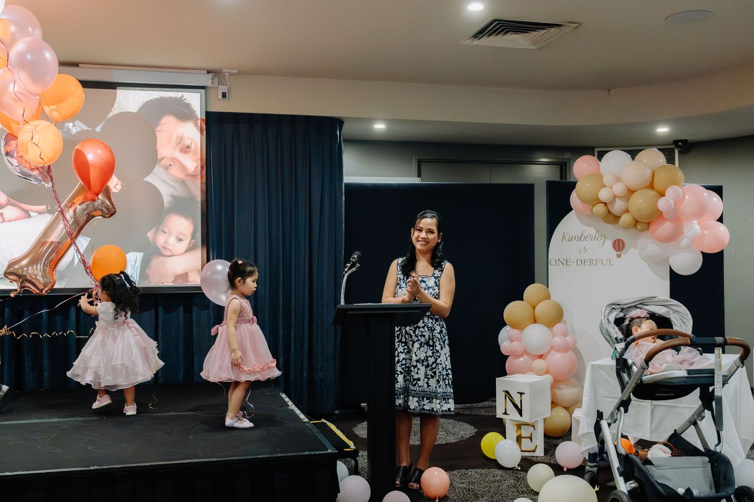 Event celebration with balloons in peach and gold colors features dancers on stage and decorative backdrop.