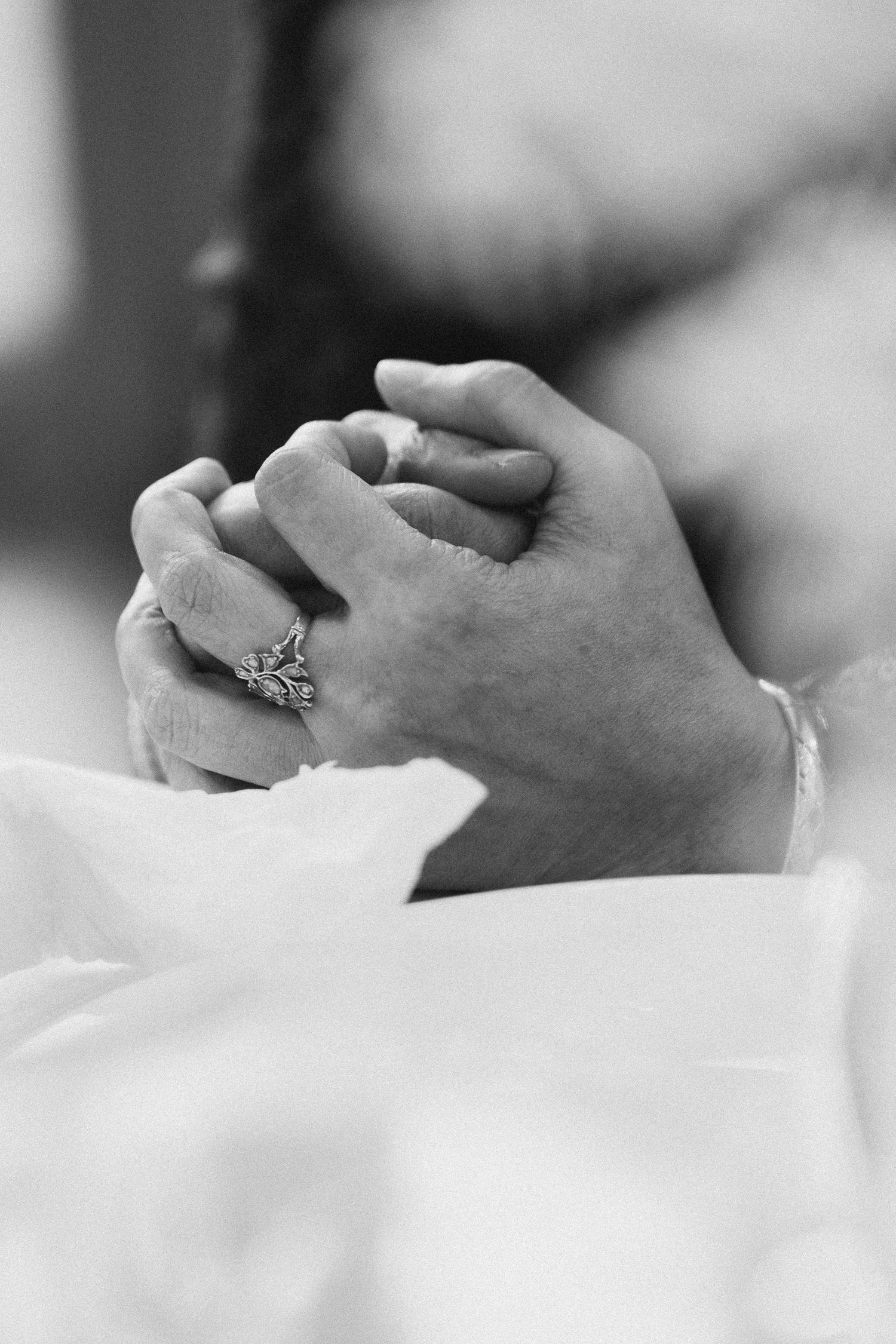 Black and white close-up of newlywed couple holding hands with ornate engagement ring visible.