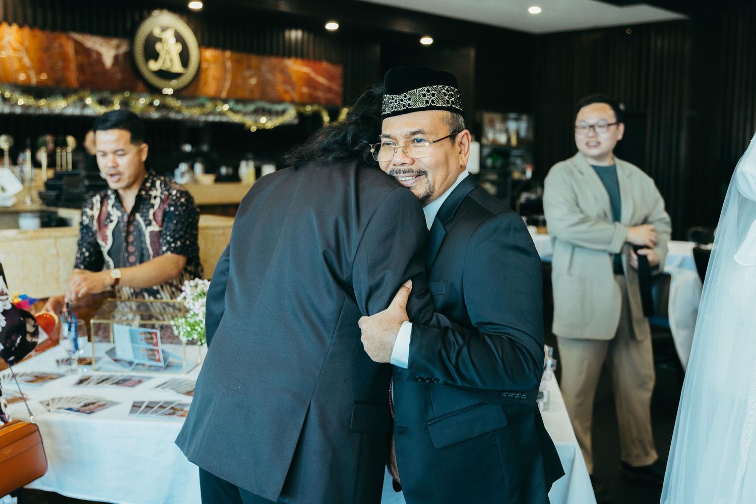 Two men in formal attire share a warm hug at an elegant wedding reception venue.