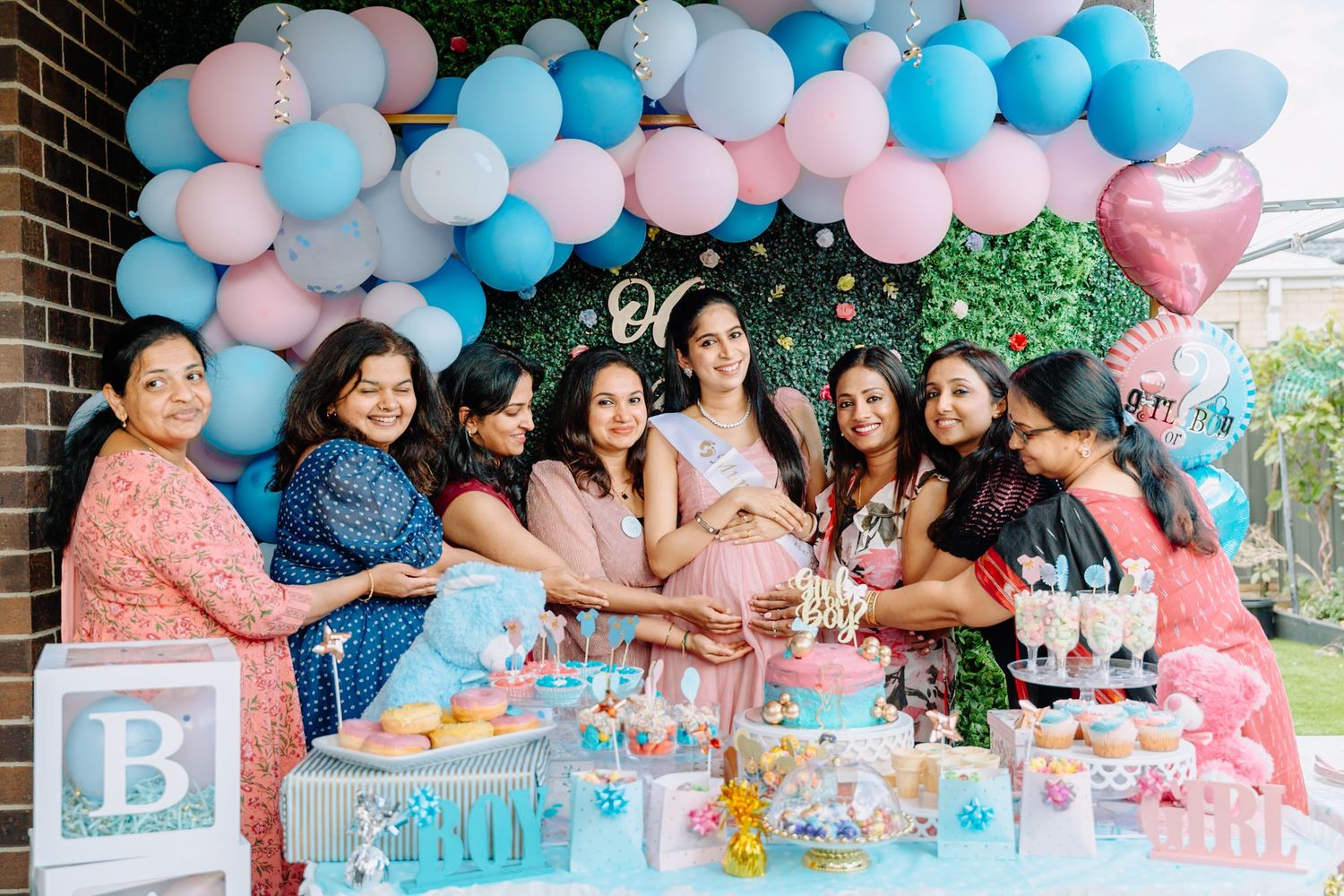 Large group gathered at gender reveal party with pink and blue balloon arch decorations.