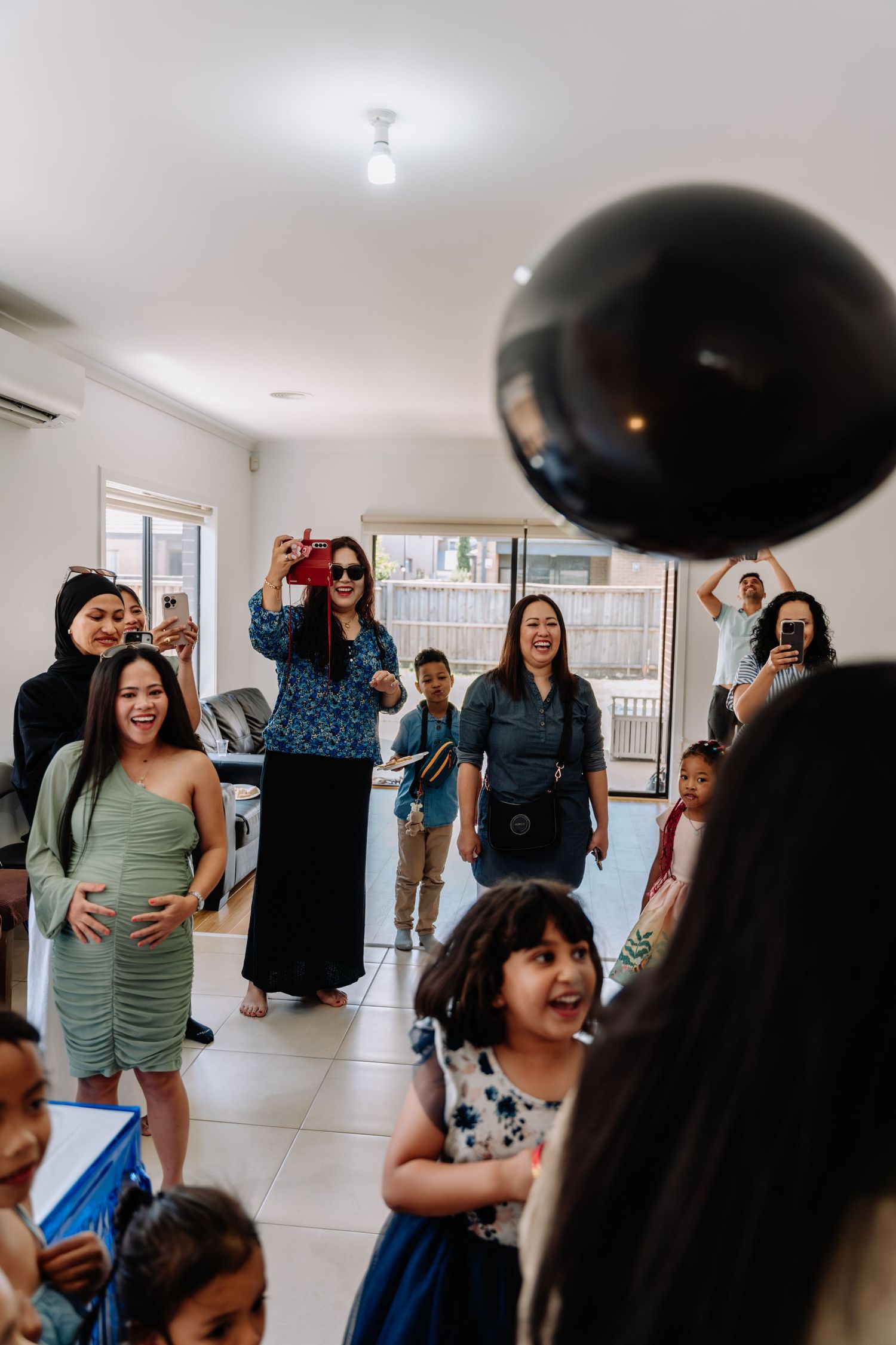 A group celebrates at an indoor party with a large black balloon floating above them.