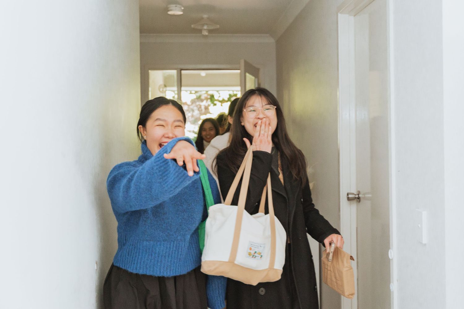 People in a hallway stand in a line with food and drinks while waiting to enter a room.