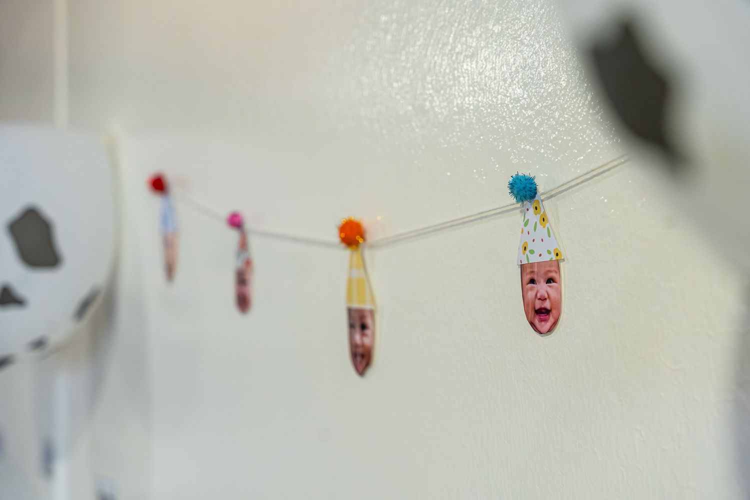 Colorful paper decorations and small ornaments hanging from a string against a white wall create a festive display.