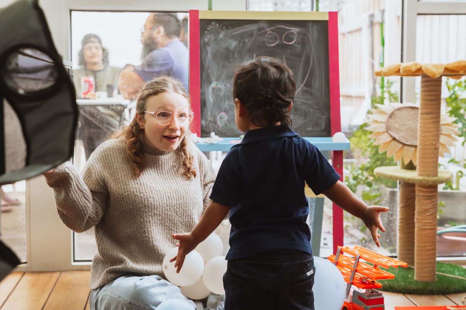 Two people share an animated moment while interacting in a casual indoor setting with natural lighting.