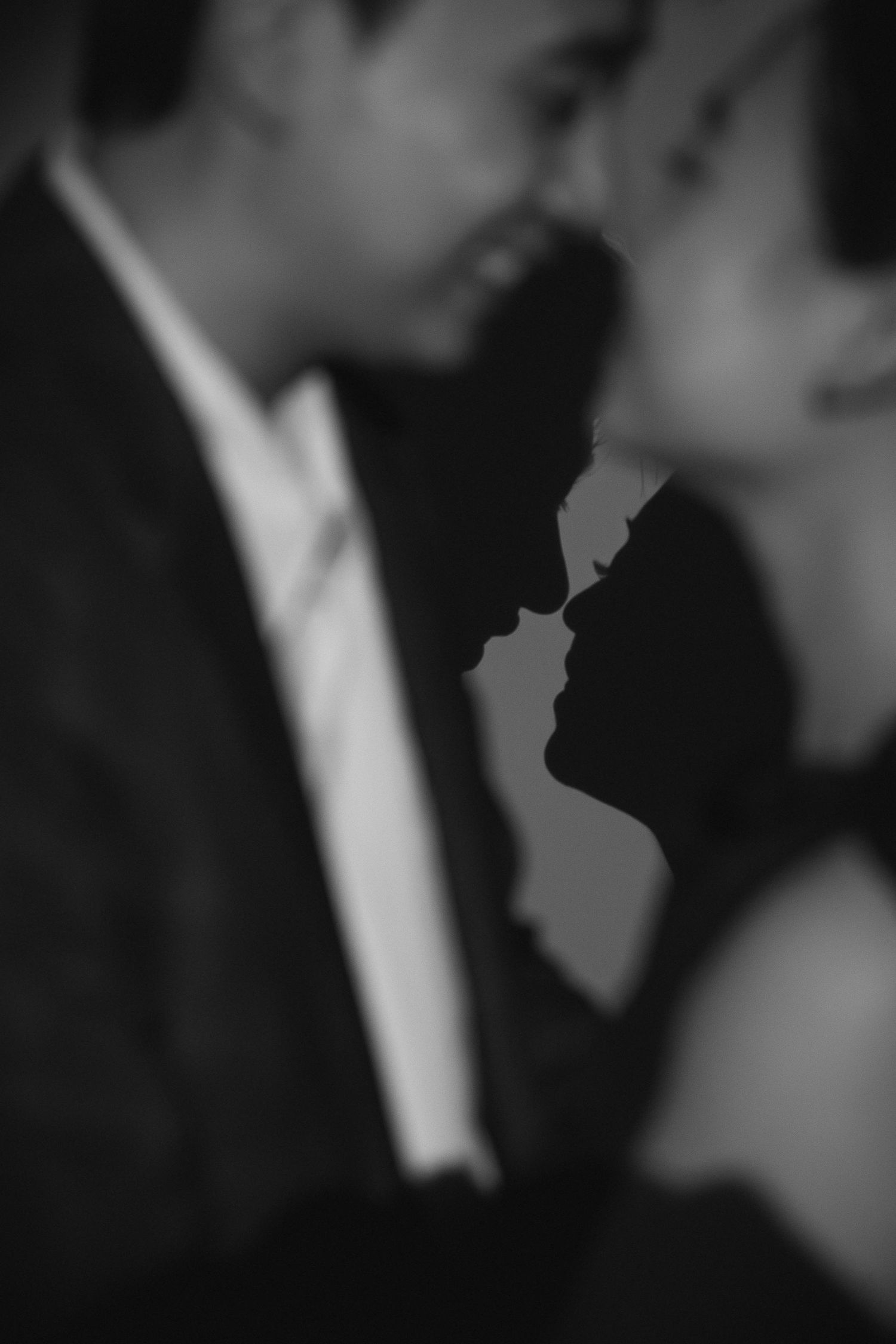 Black and white silhouette of a romantic couple about to kiss, with blurred figures in the background.