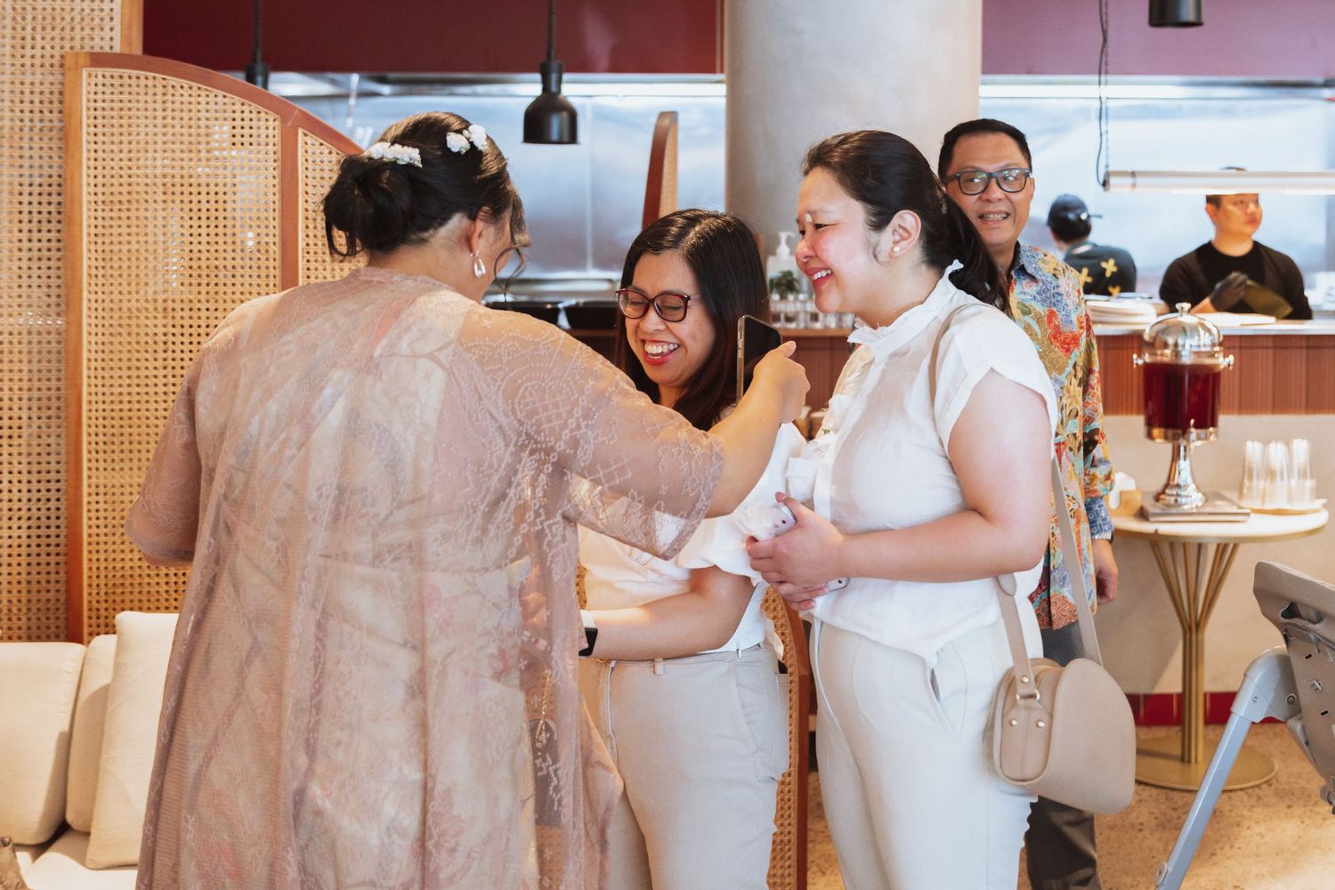 Guests in white attire mingle and socialize at an elegant indoor event with warm lighting and cream-colored decor.