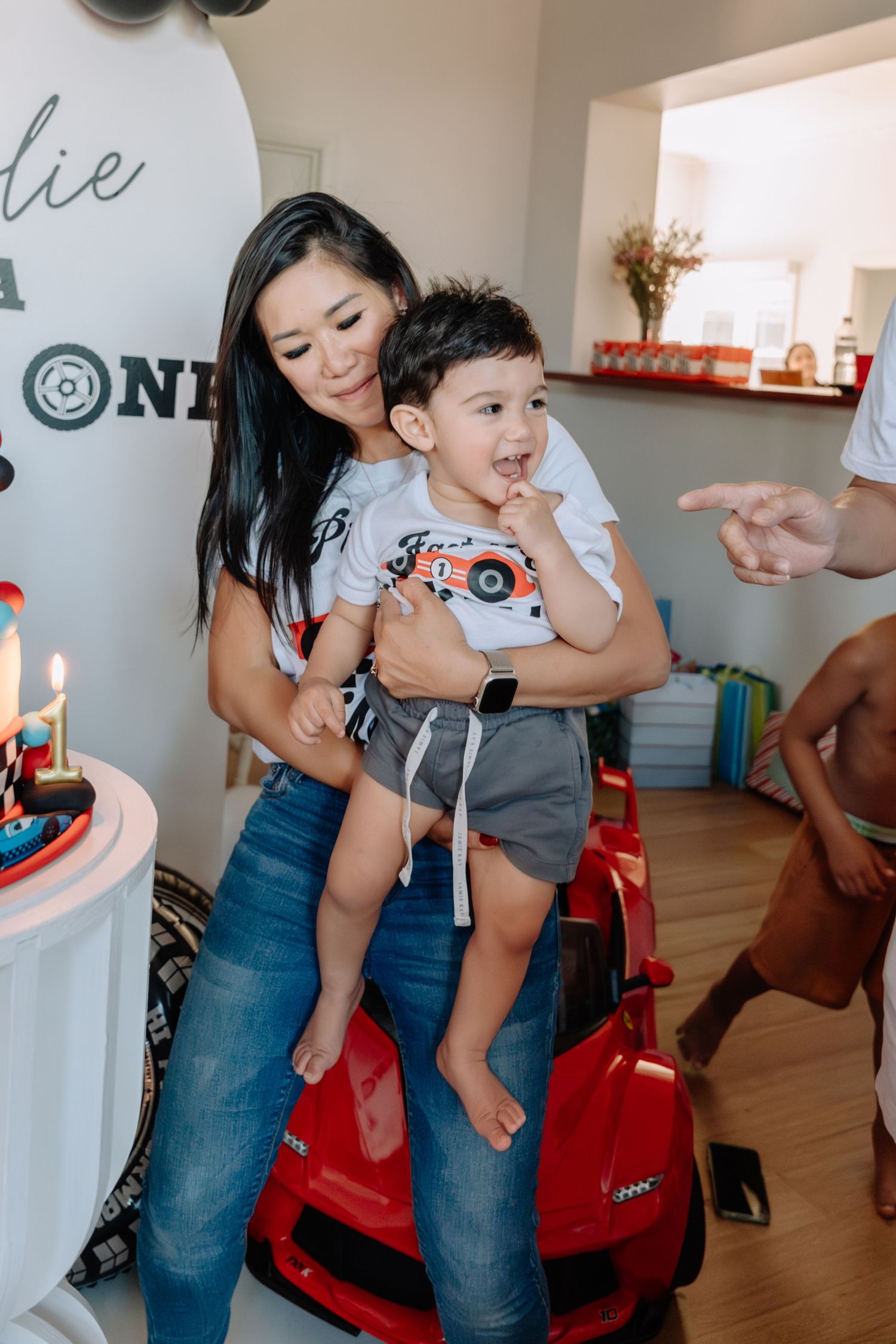 Racing-themed party scene with red toy cars and casual attire indoors.