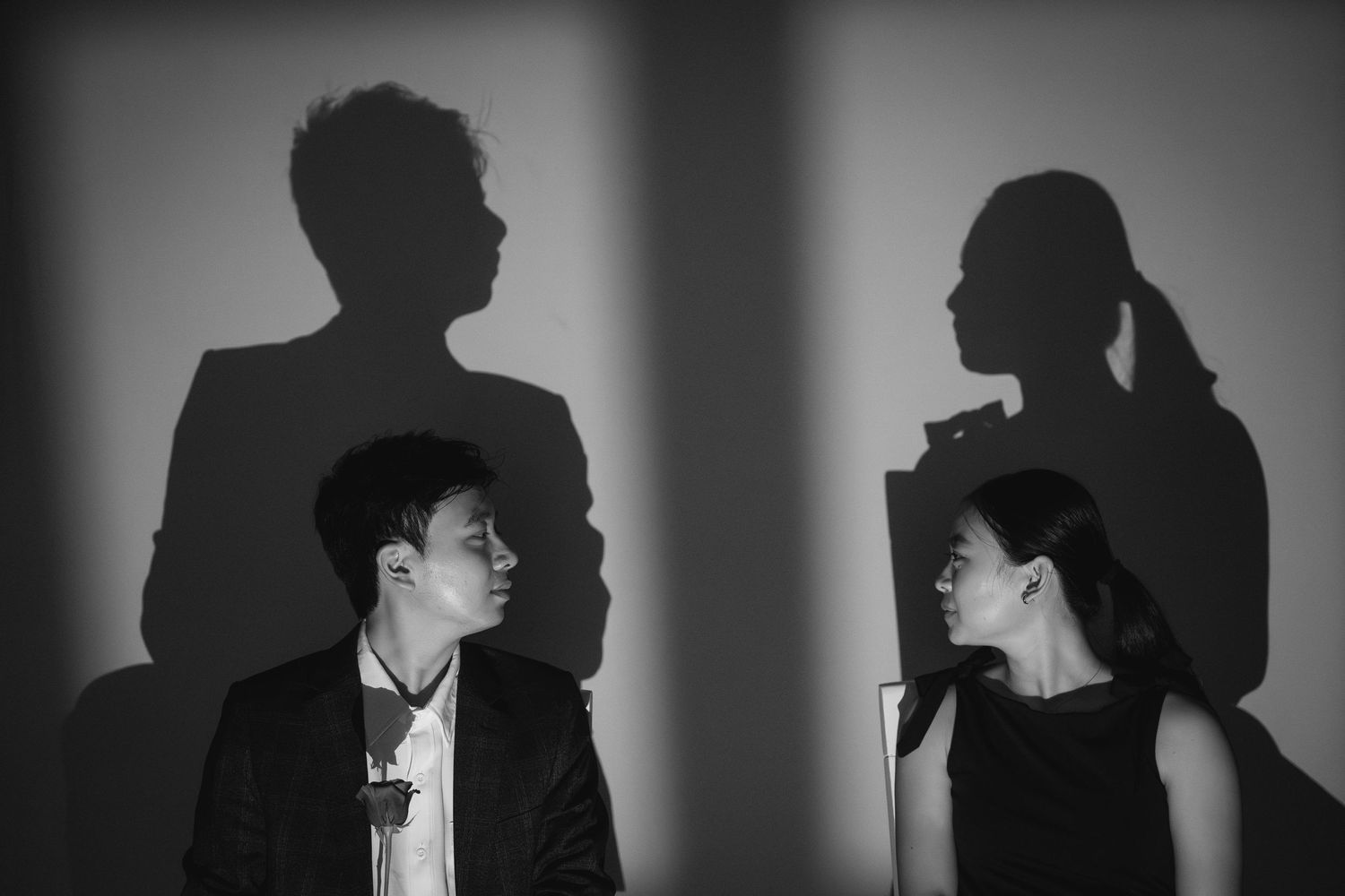 Black and white photo of a couple facing each other with dramatic shadows on the wall behind them.