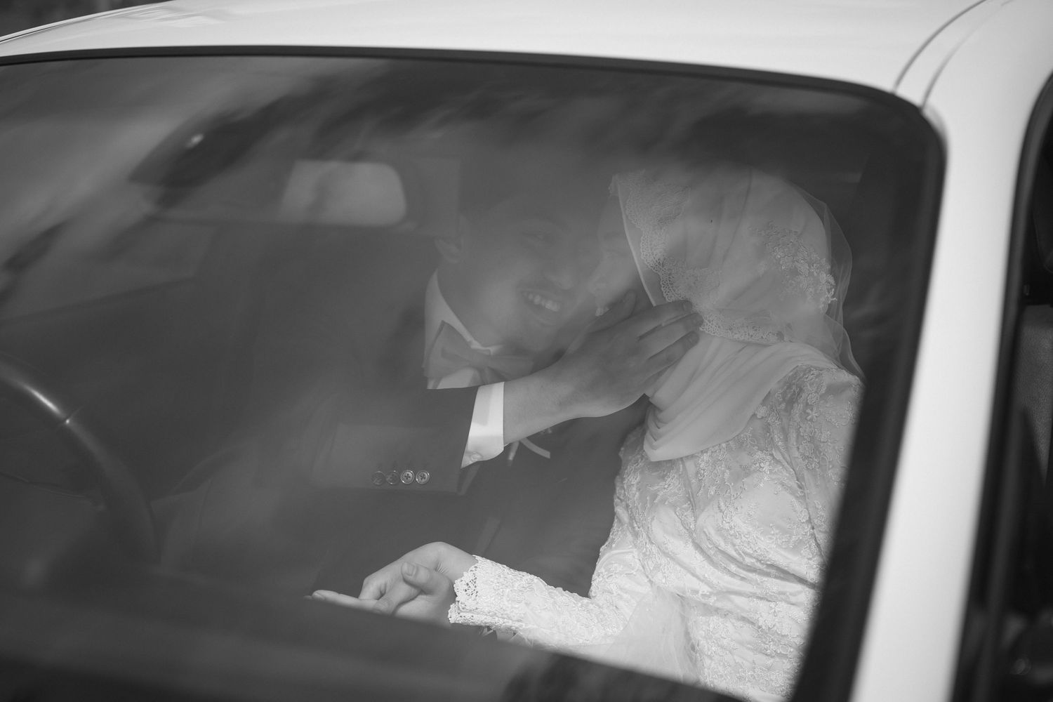 Black and white photo of bride and groom sharing an intimate moment inside a wedding car.