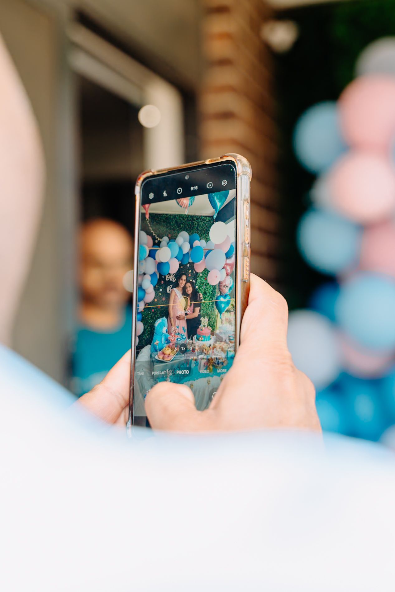 Smartphone capturing photo of gender reveal party celebration with balloon decorations.