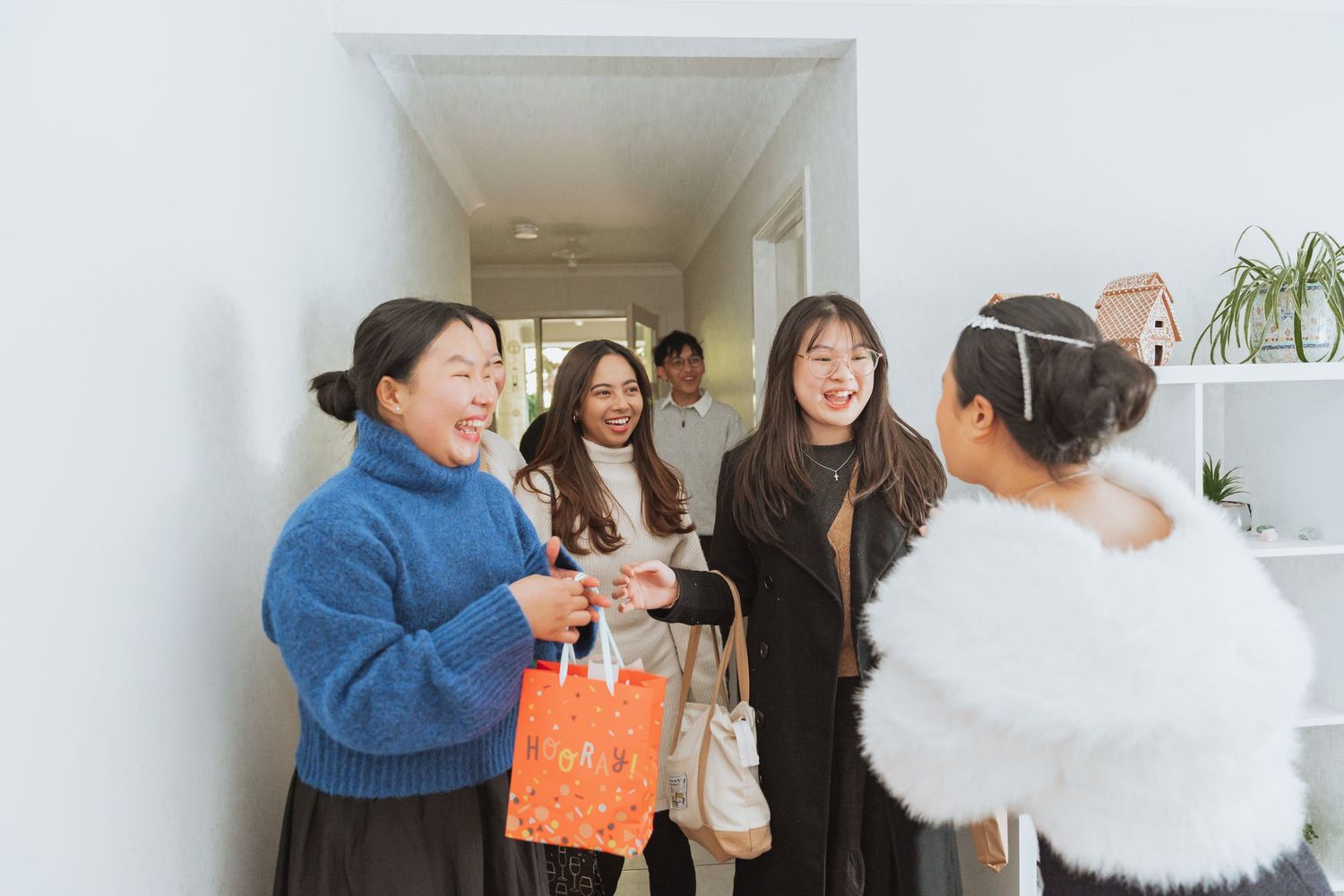 A group of friends laughing together in a bright hallway while holding shopping bags and wearing winter sweaters.