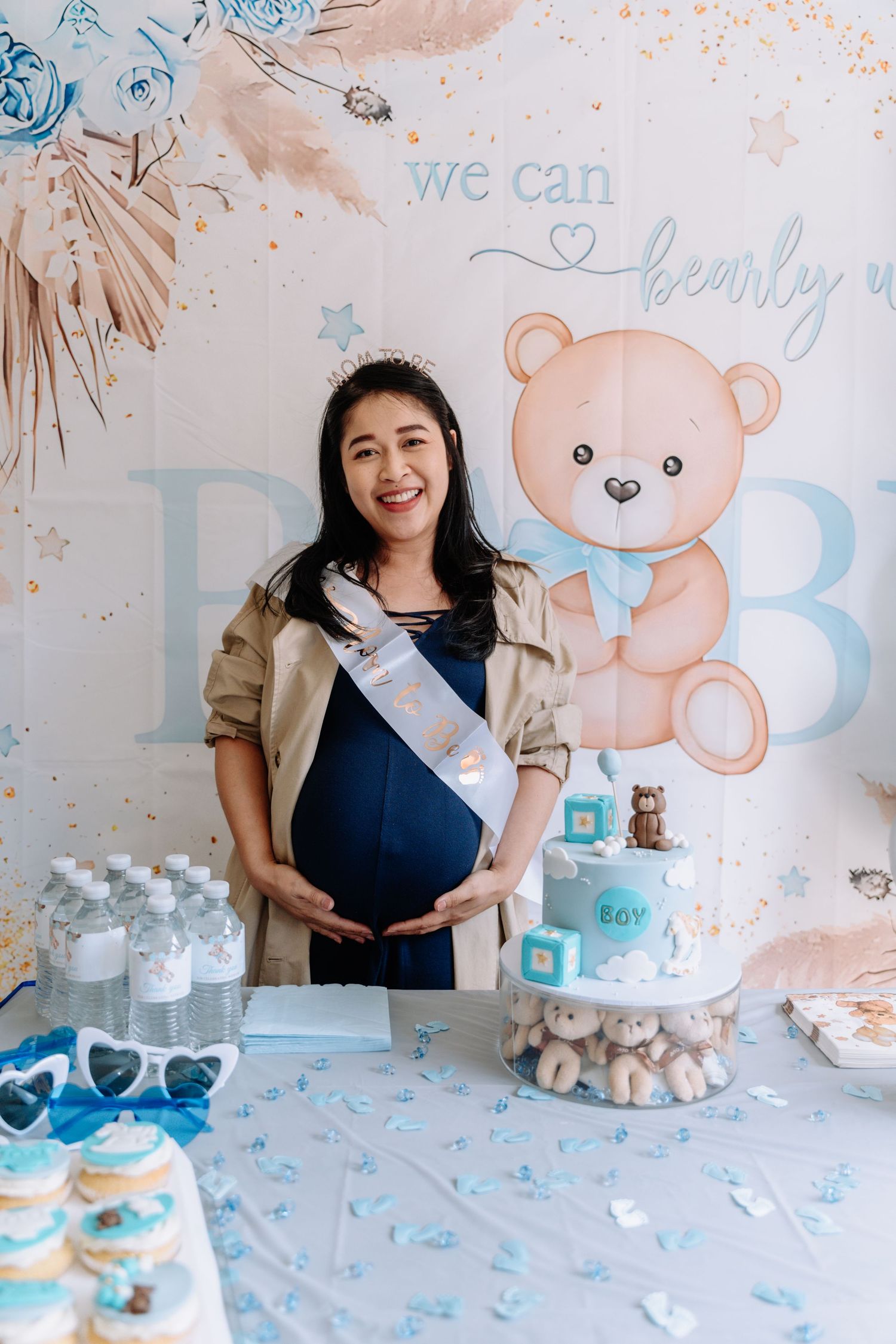 A baby shower celebration setup with blue and pink teddy bear decorations and treats on a white table.
