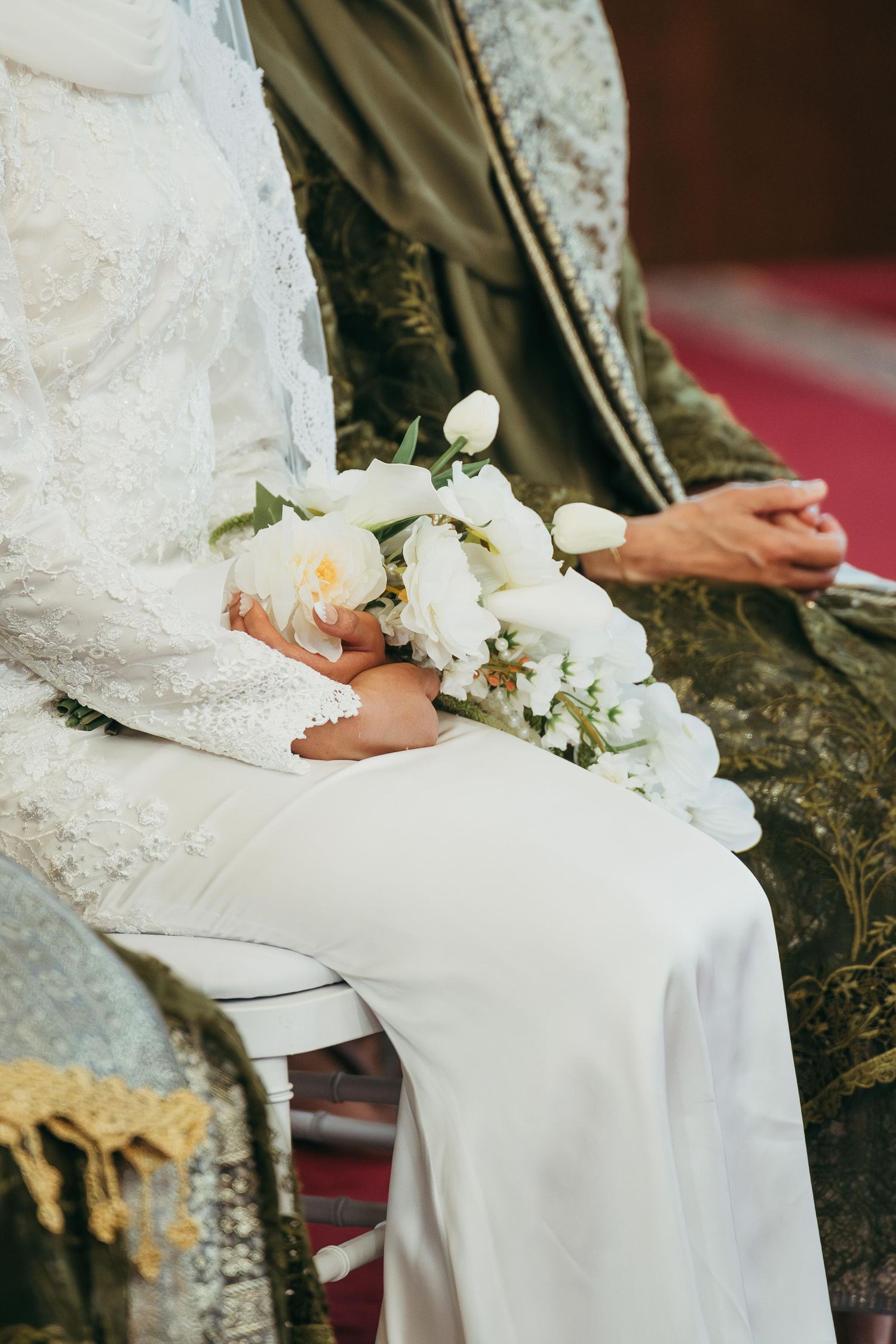 Bride in white lace dress holding bouquet of white peonies at wedding.