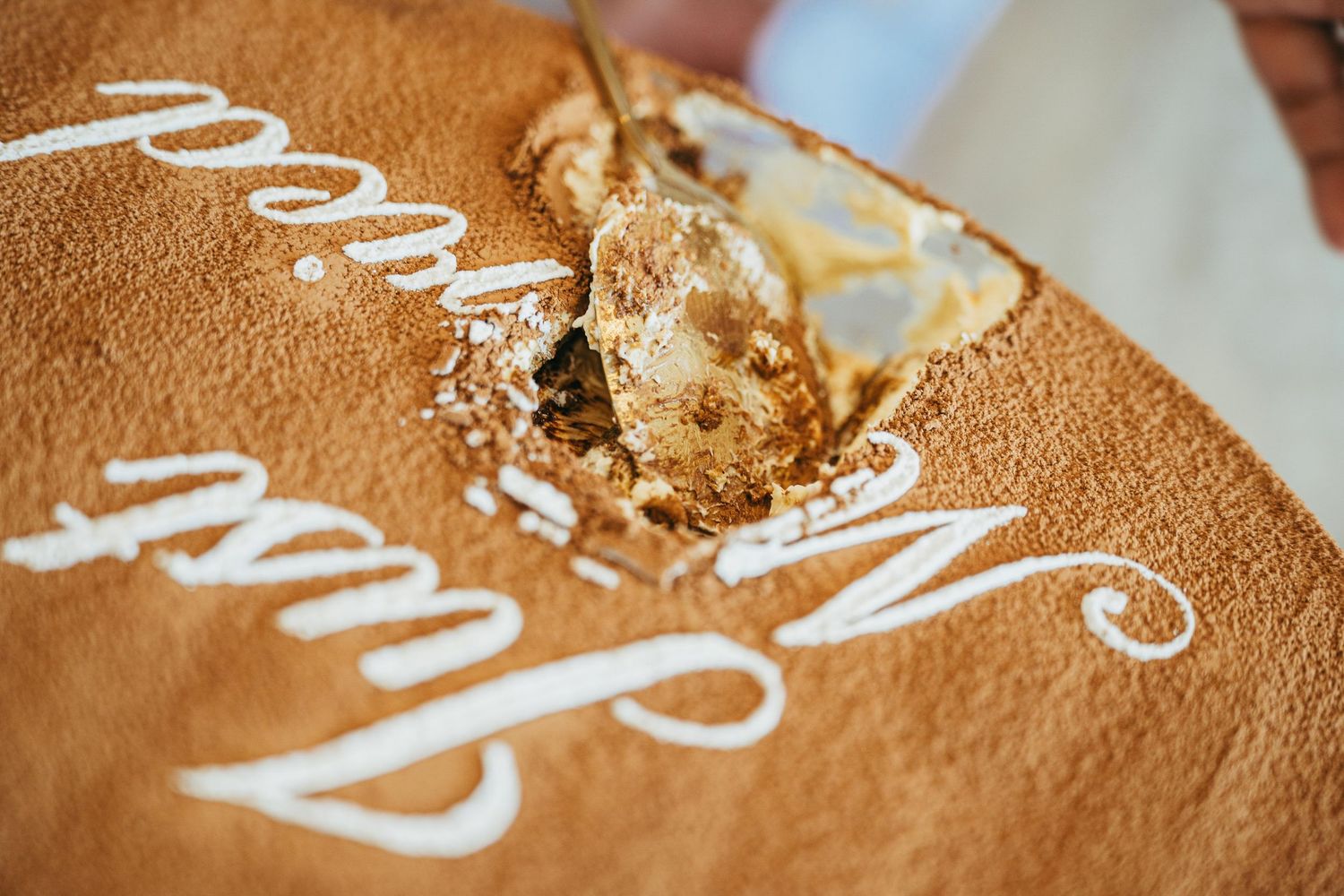 Close-up of ornate wedding cake being cut with decorative script lettering on top.