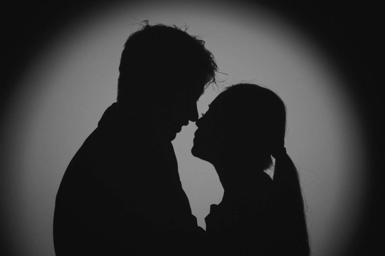 Black and white silhouette of a romantic couple facing each other in a spotlight.