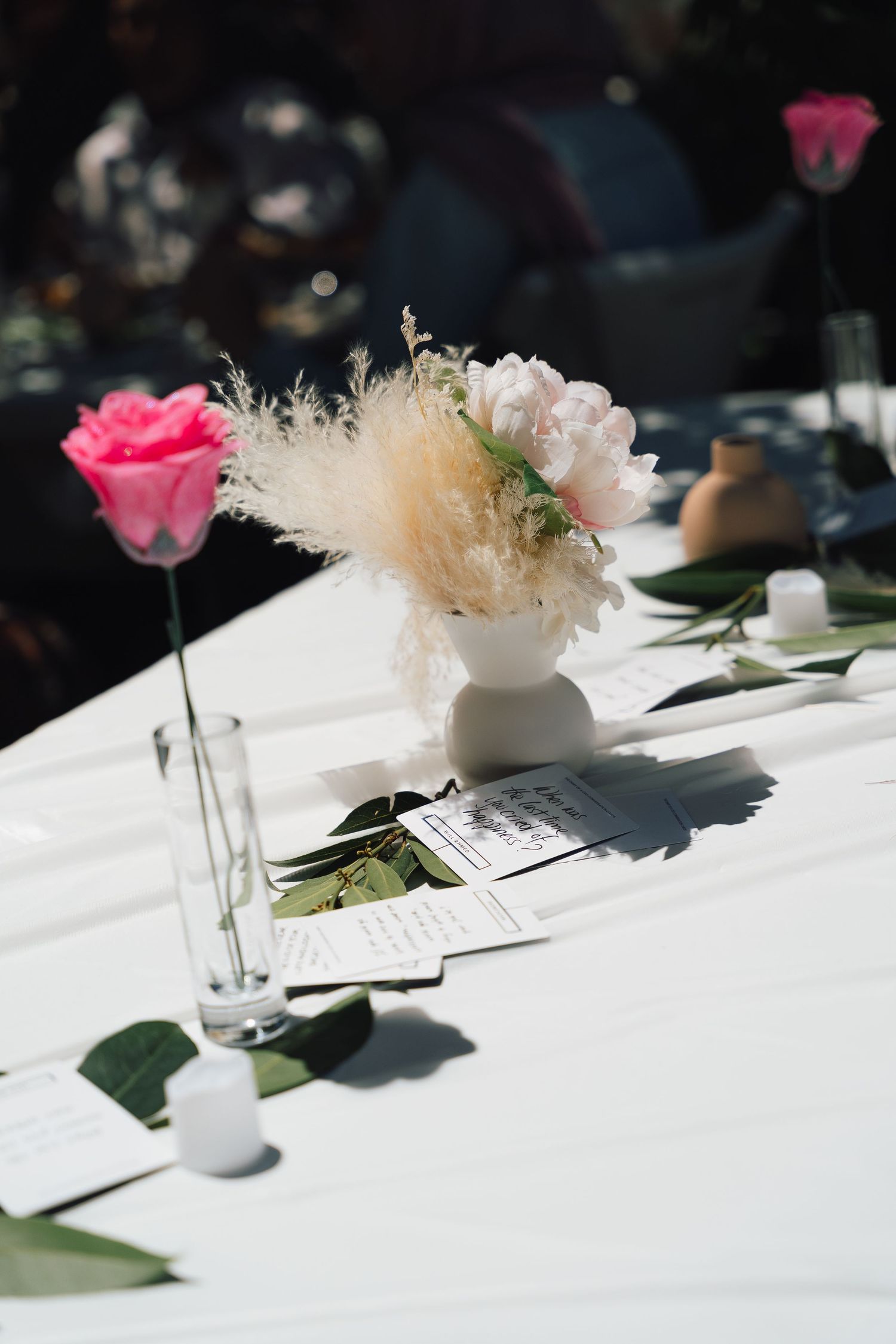 Pink roses and delicate dried flowers create an elegant table setting with white linens and place settings in natural light.
