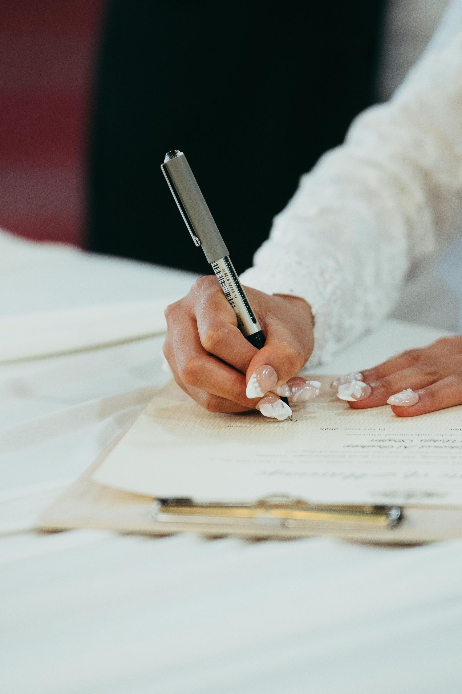 A bride with decorated nails signs wedding documents with a pen during a marriage ceremony.