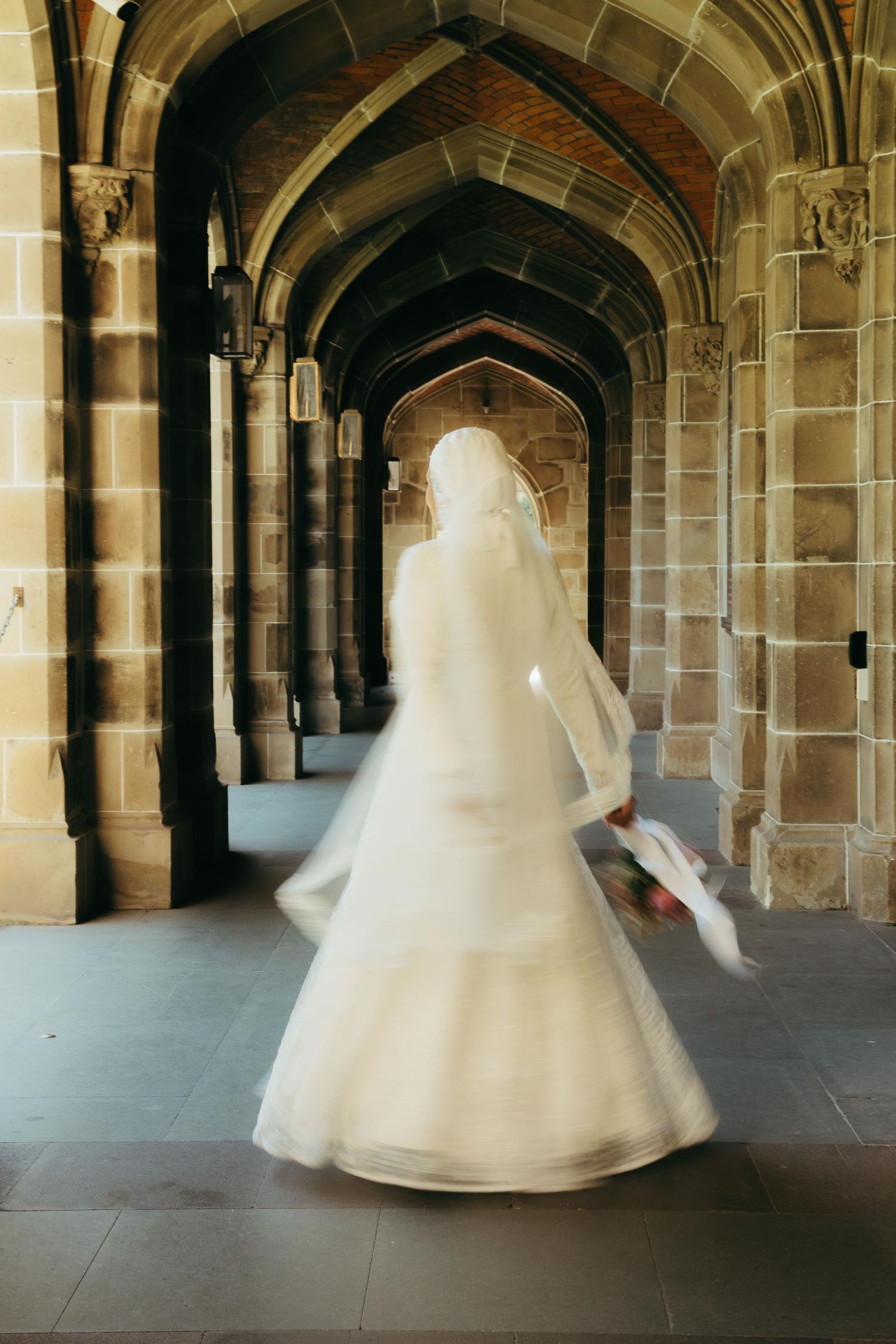 Bride in white wedding dress and veil spinning in Gothic stone archway corridor, motion blur effect.