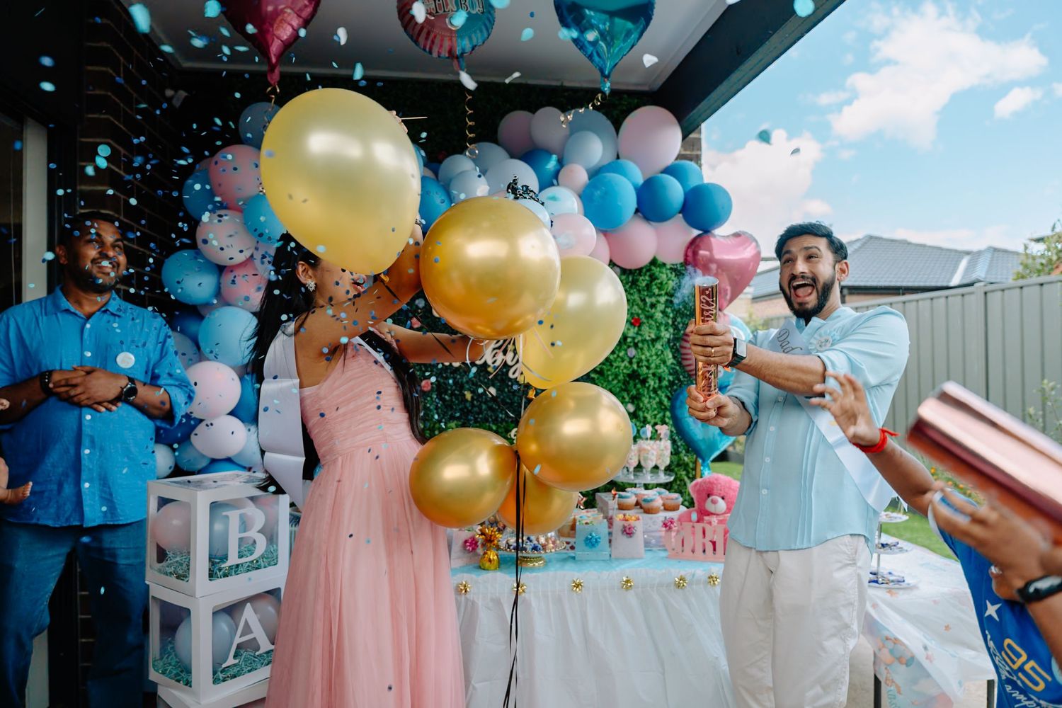 Outdoor gender reveal celebration with pink and blue balloon arrangements and party decor.