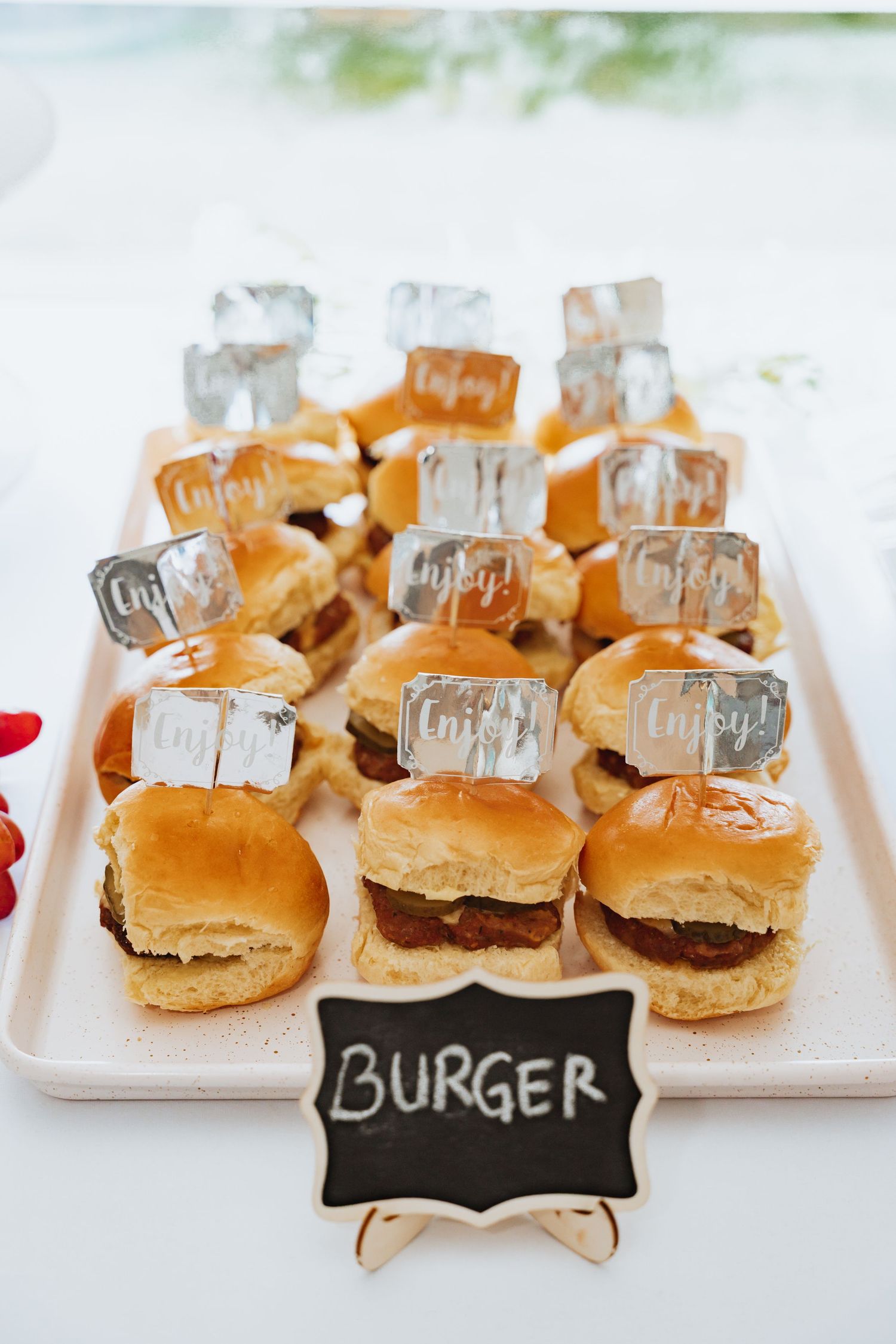 Close-up of slider burgers arranged on white plates with a black chalkboard sign.
