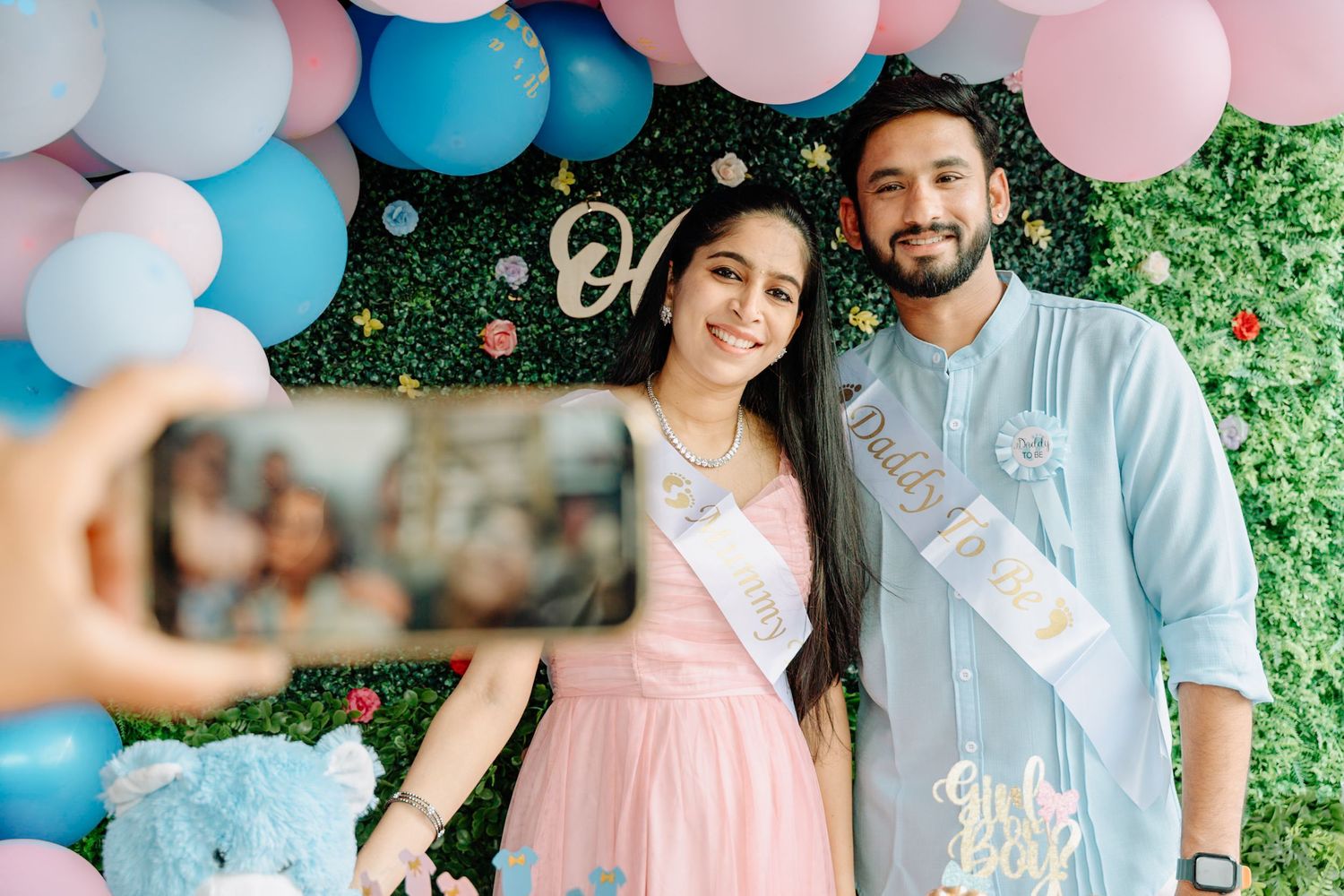 Gender reveal party setup with blue and pink balloon decorations against a brick wall backdrop.