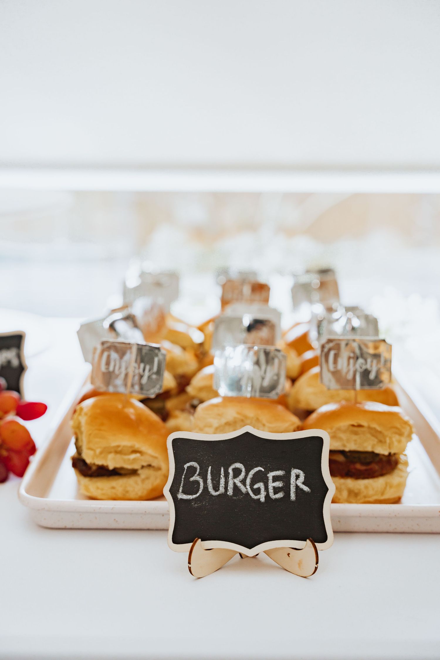 Mini burgers on white serving plates with a decorative black chalkboard label.