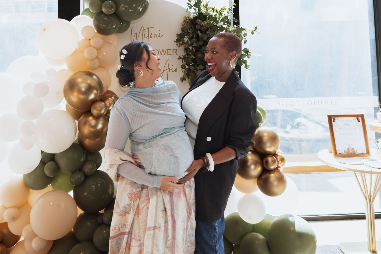 Wedding celebration with white and olive green balloon arch decorations in a bright venue with large windows.