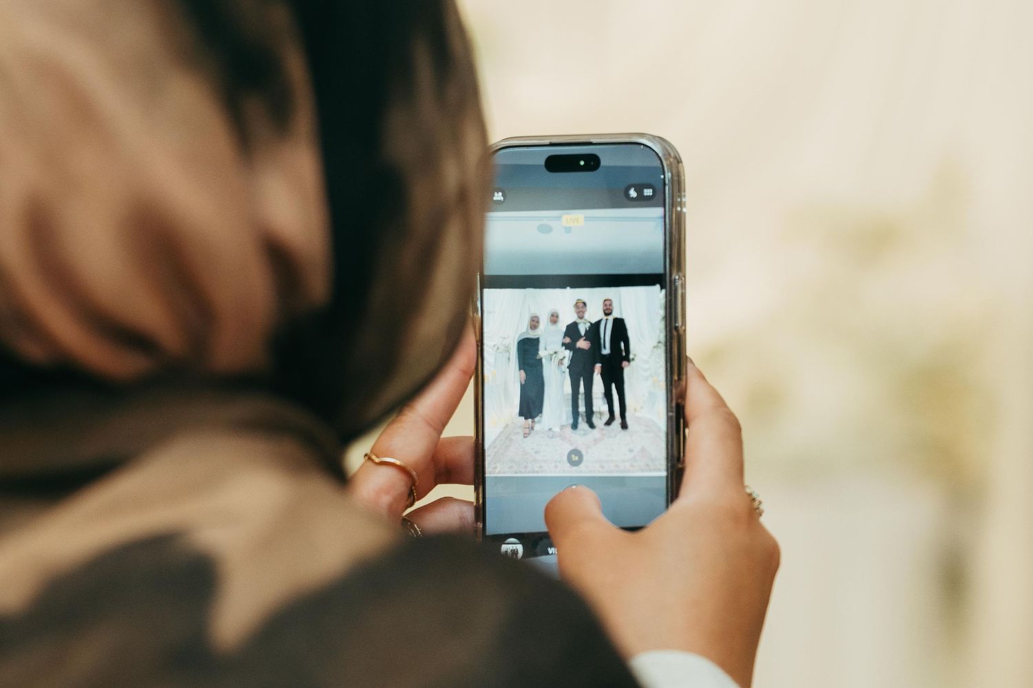 A woman photographs a group of formally dressed people at a wedding event using her smartphone.
