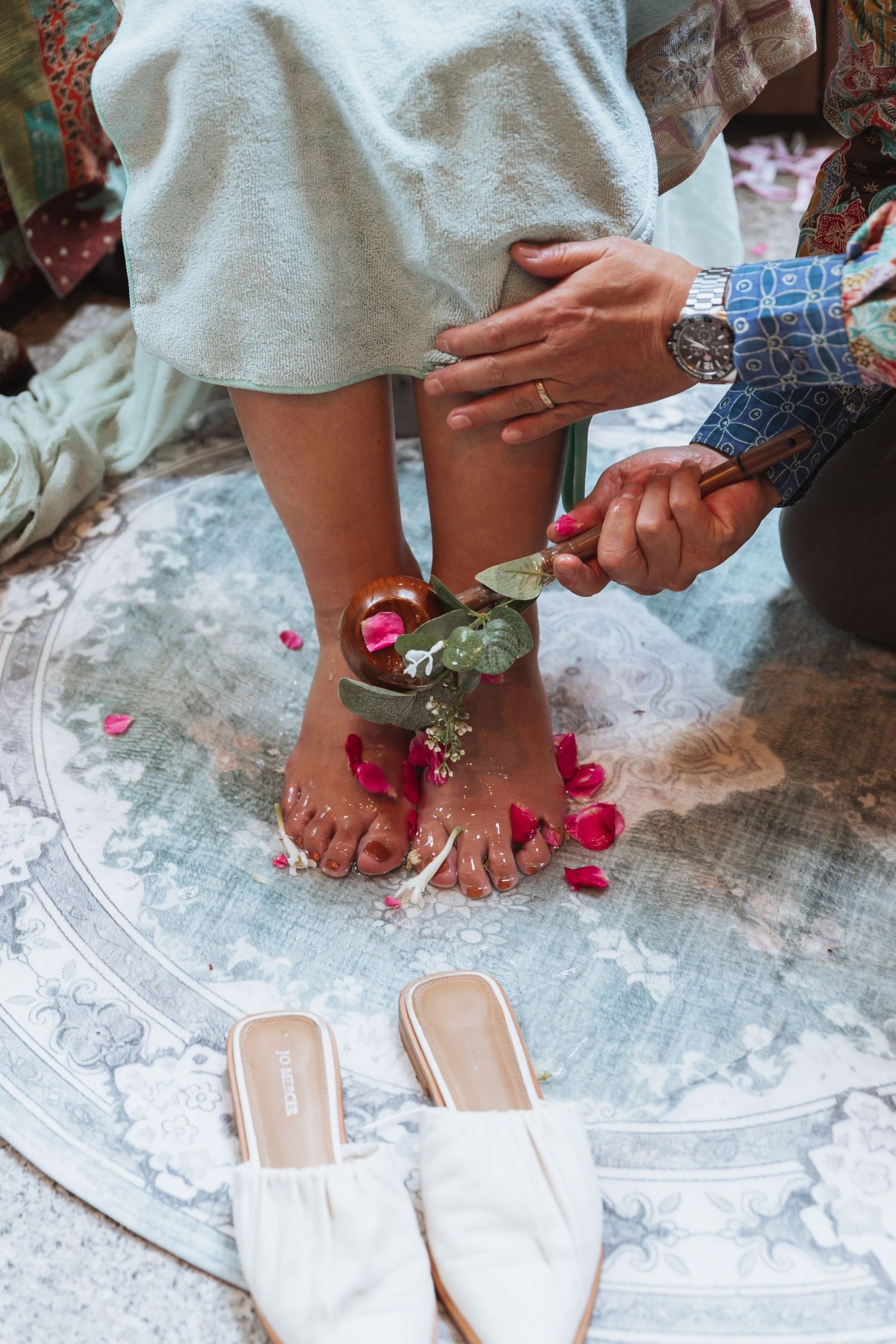 Close-up of feet being adorned with rose petals during a wedding ceremony on a decorative rug.