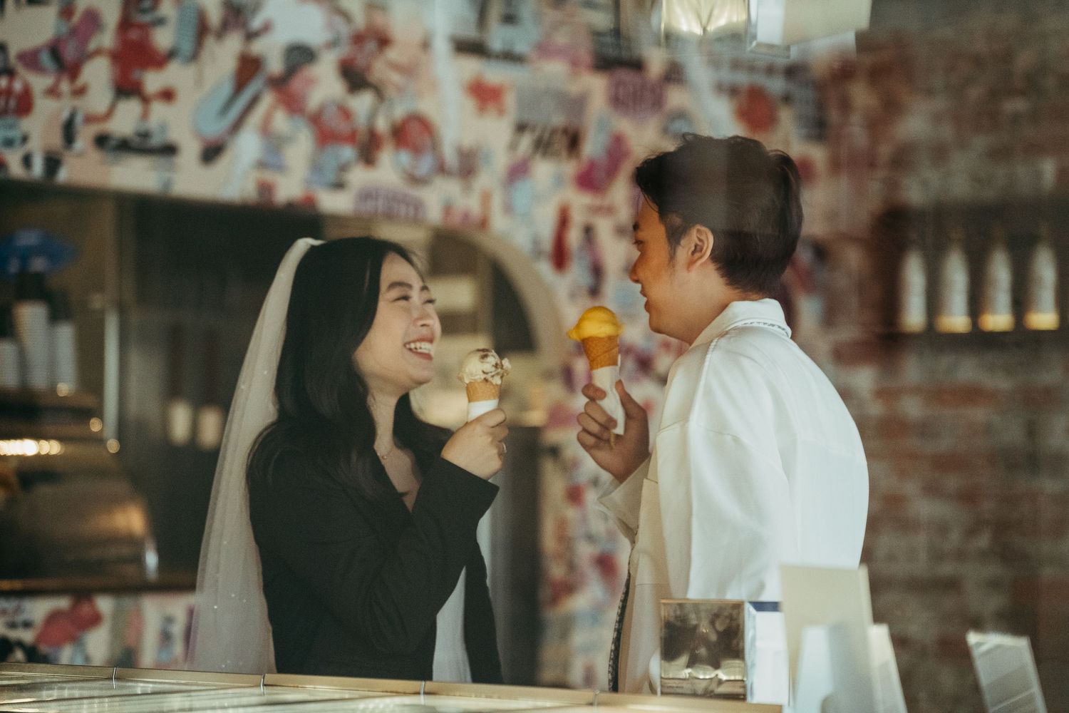 Two people sharing ice cream and laughing together inside a colorfully decorated restaurant.