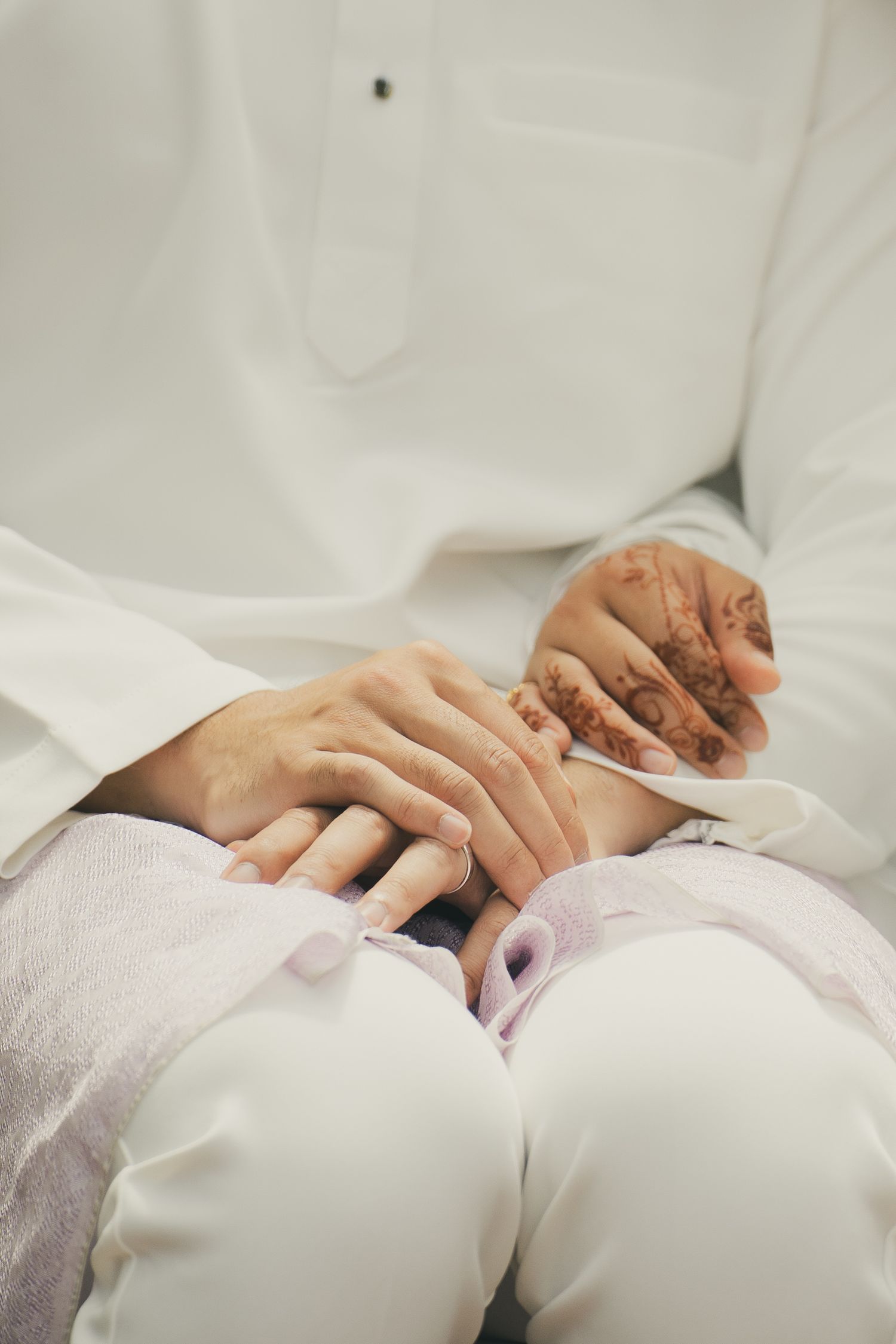 Close-up of a couple holding hands with henna tattoos, dressed in white traditional wedding attire.