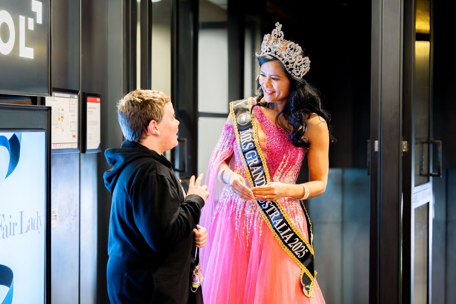 Beauty pageant contestant wearing a pink ball gown and crown in an elegant venue.