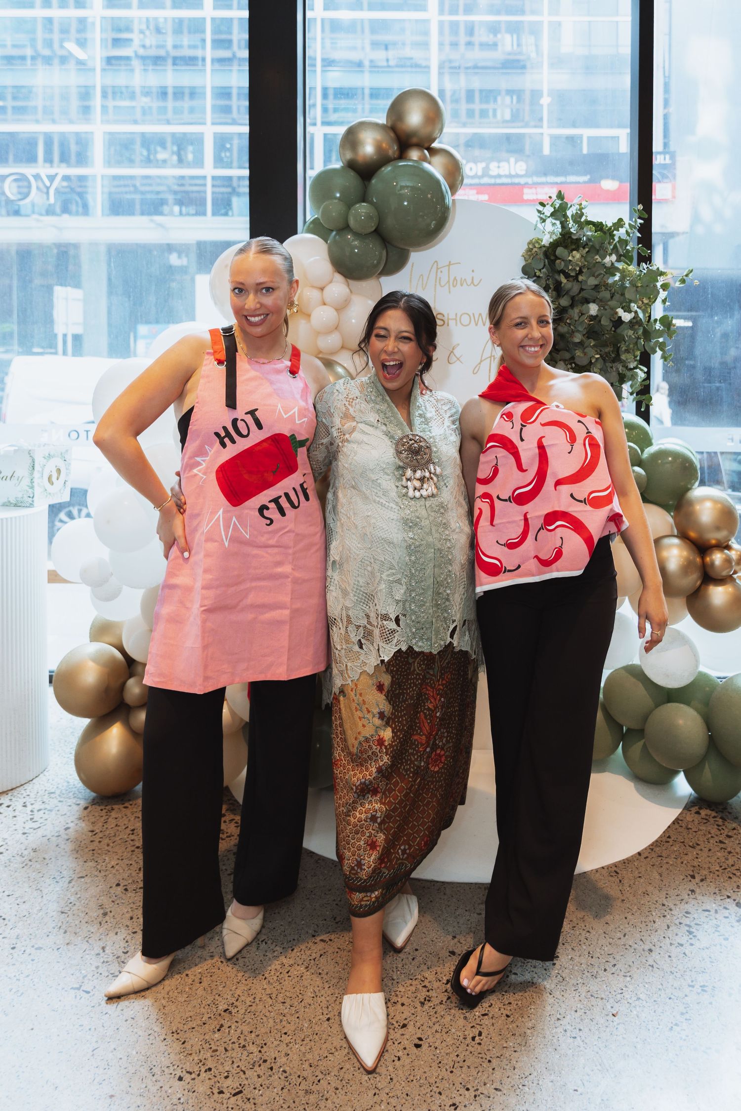 Group wearing matching pink and black outfits pose in front of balloon arch and window backdrop.