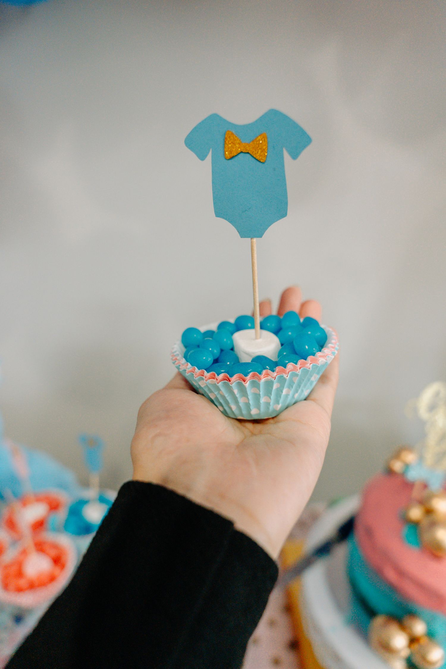 Small blue onesie-shaped cake topper or decoration held against a light background.