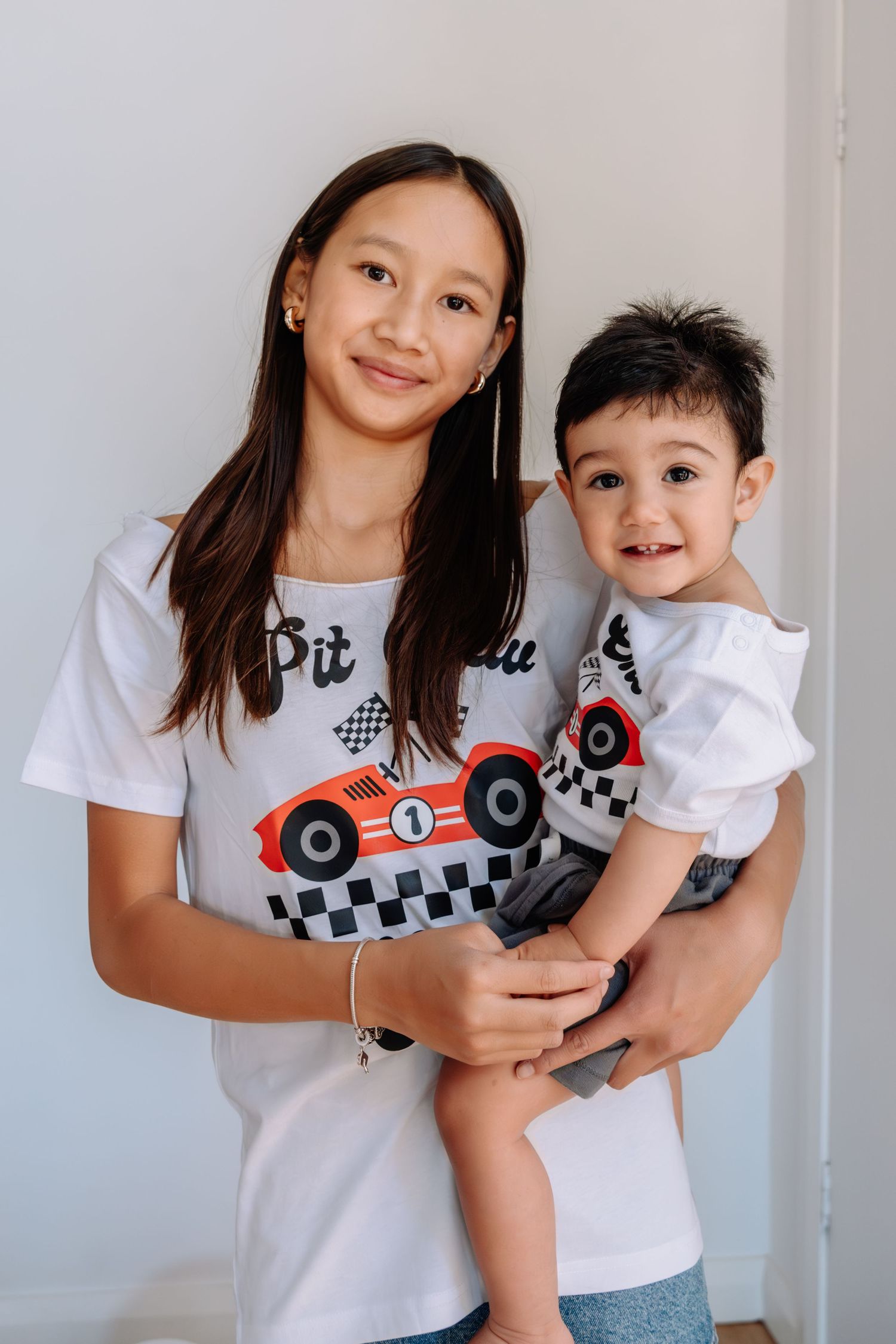A parent and child wearing matching white t-shirts with race car designs smile together in a casual indoor portrait.