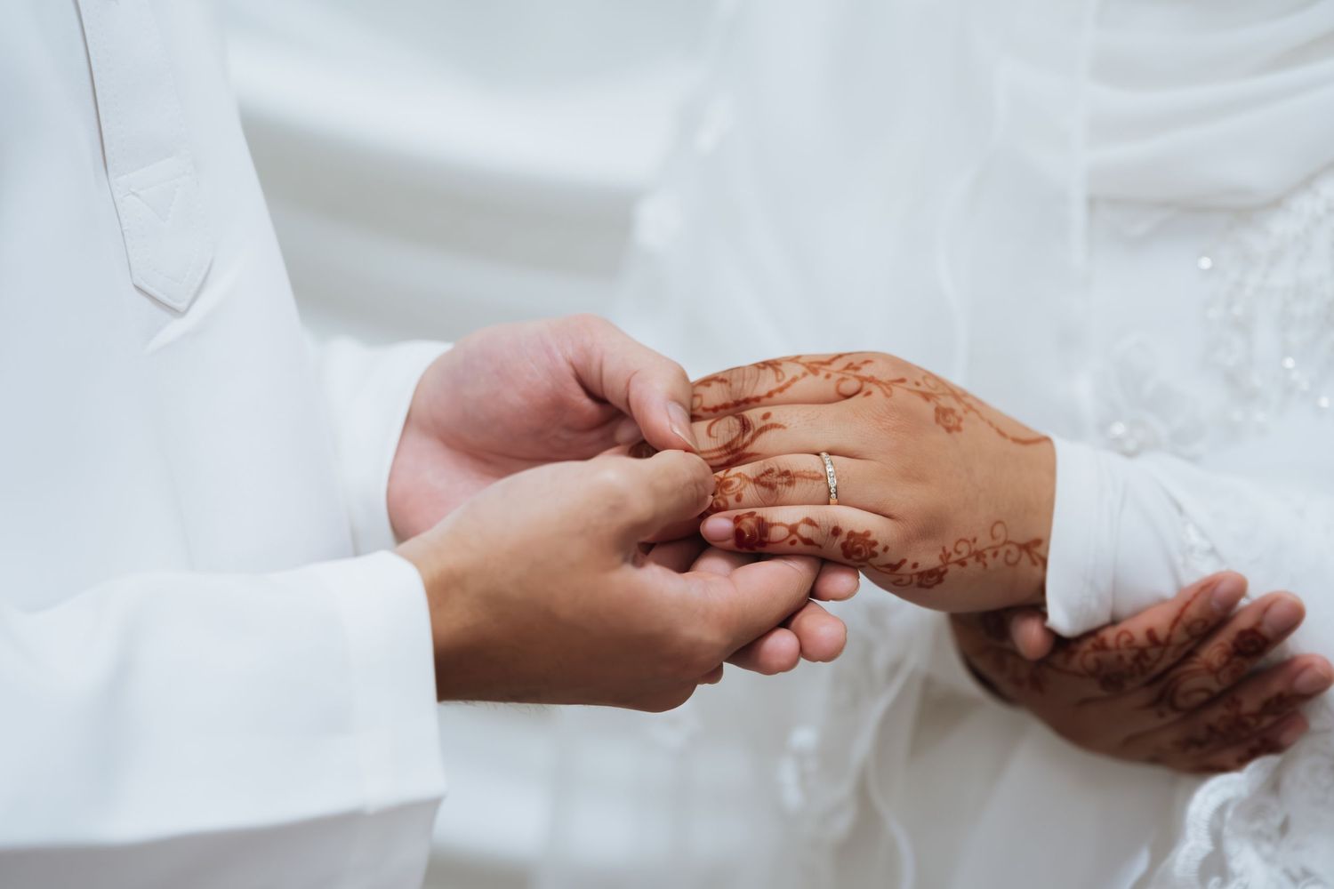 Groom placing a ring on bride's henna-adorned hand during a traditional Muslim wedding ceremony.