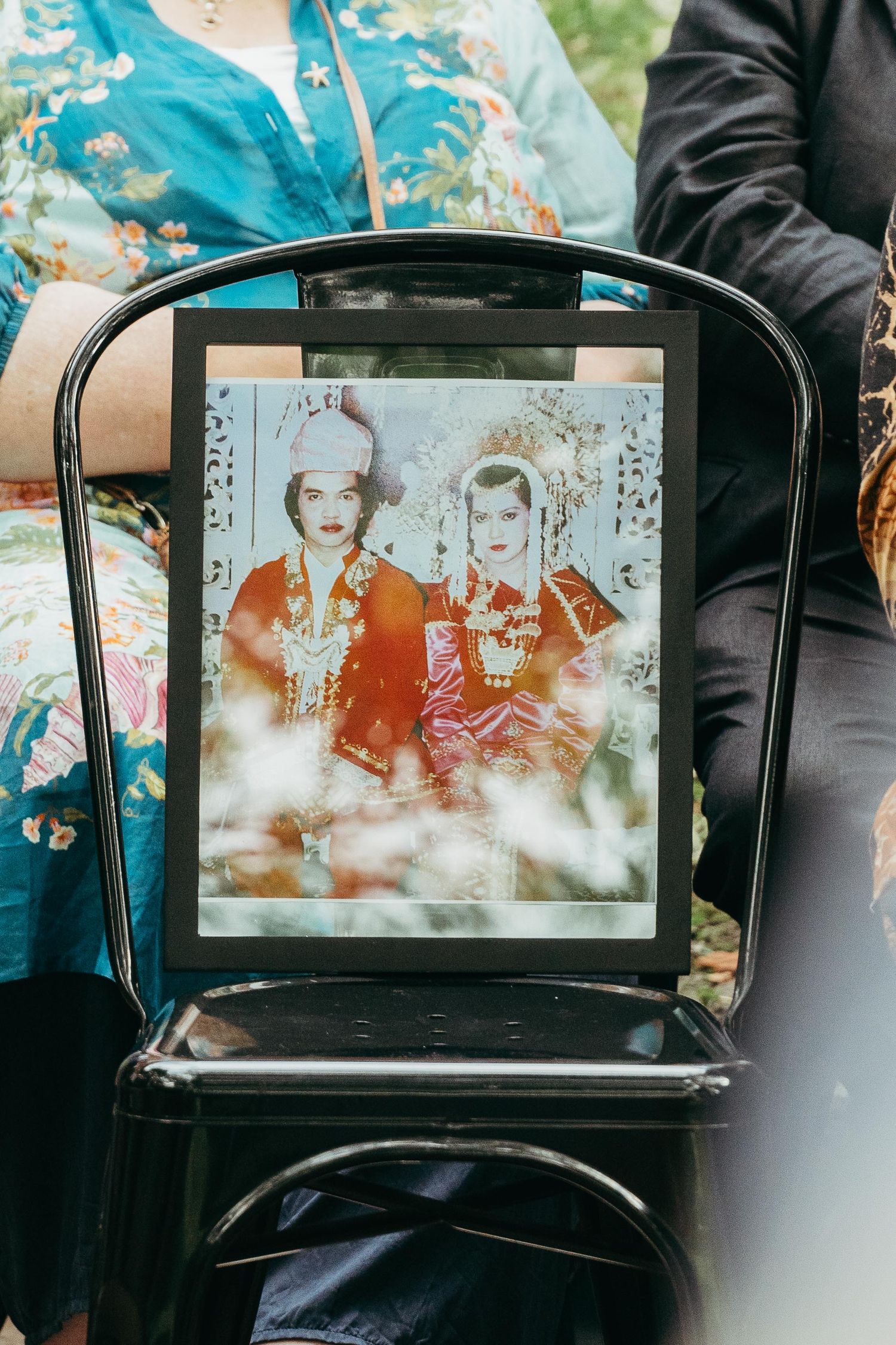 Framed vintage wedding photo of couple in traditional Indonesian attire displayed on black chair at ceremony.