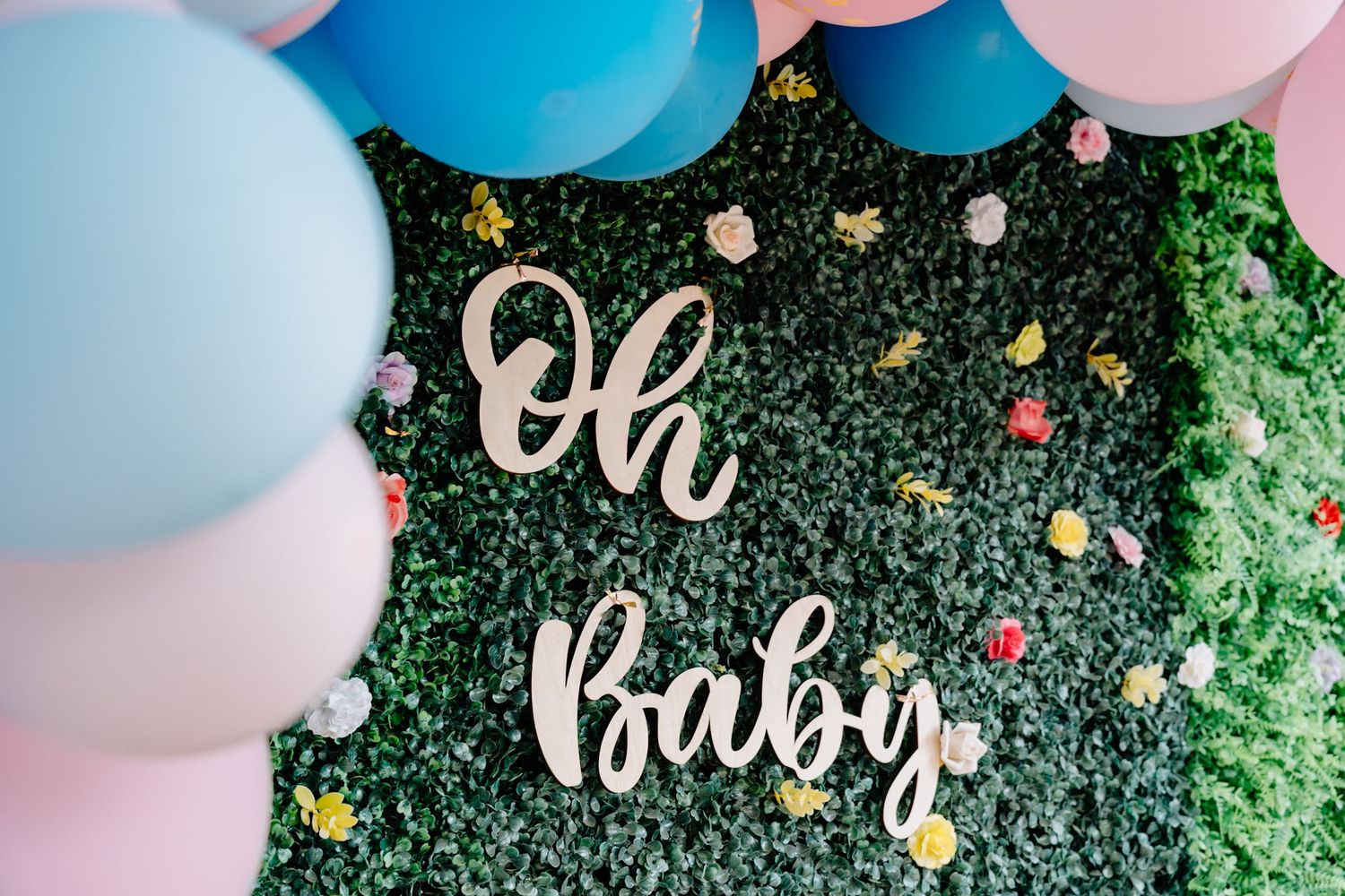 Pink and blue balloon arch with greenery decorations at a gender reveal party celebration.