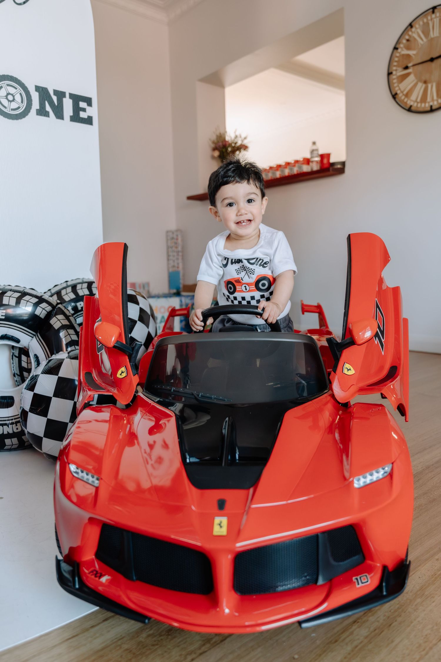 A red toy Ferrari LaFerrari ride-on car displayed indoors with racing decor visible in the background.