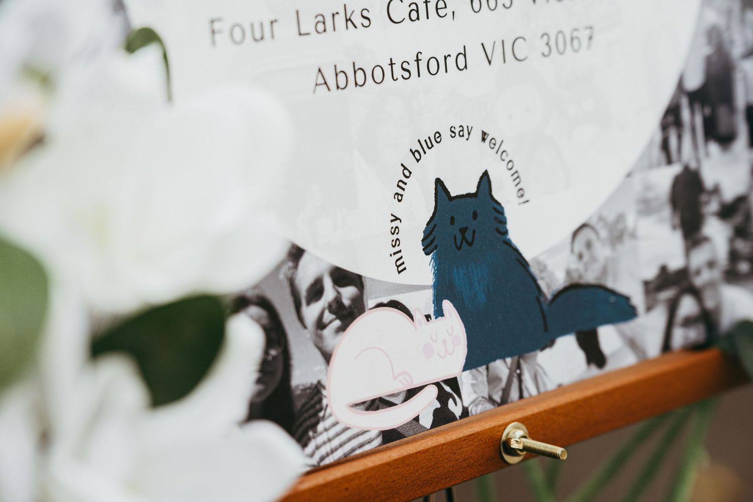 A wedding sign on an easel for Four Larks Cafe in Abbotsford VIC 3067 featuring a charming blue cat illustration.