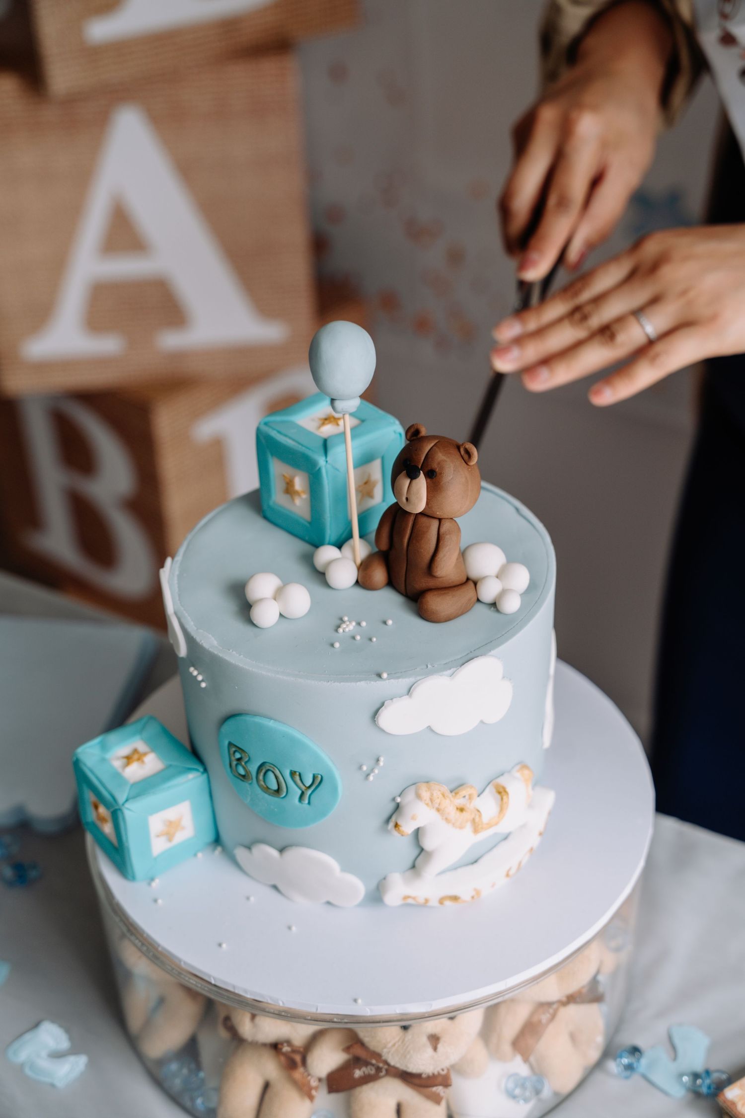 A light blue baby shower cake decorated with clouds, blocks, and teddy bear toppers.