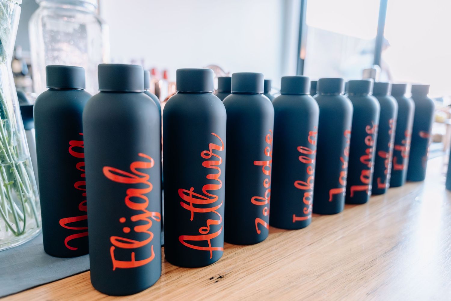 Row of black water bottles with red text displayed on wooden table surface.