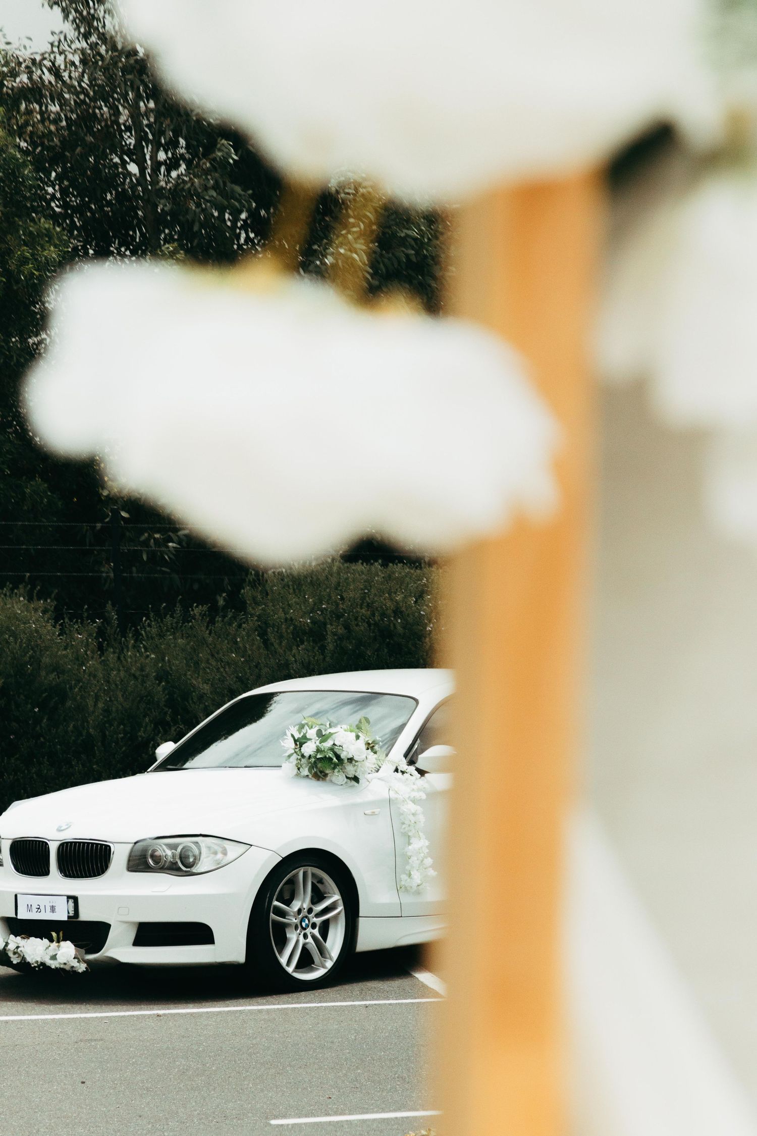 White BMW convertible wedding car decorated with flowers parked on a road.