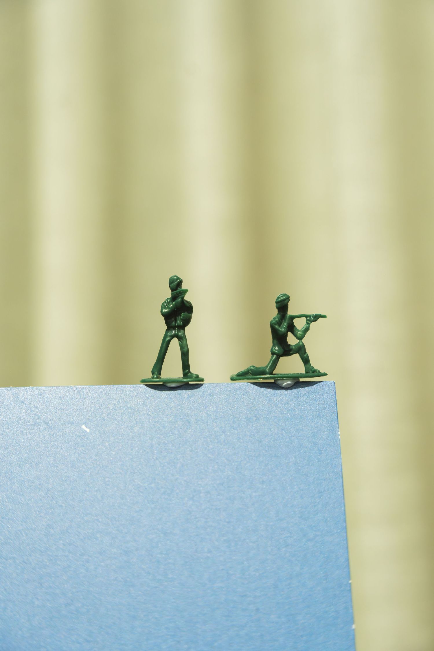 Green toy army men stand in sequence along a light blue surface against a beige background.