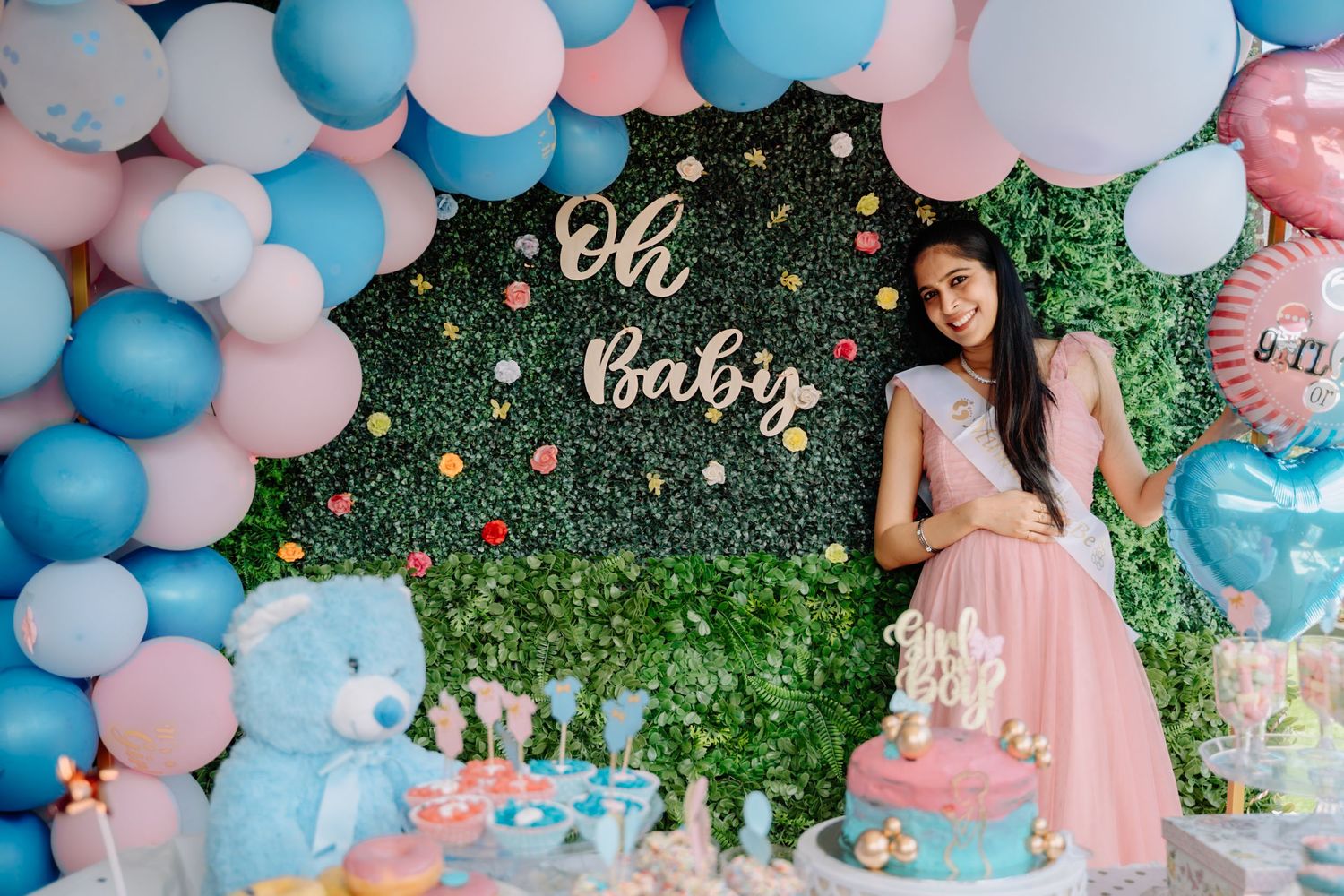Party venue decorated with pink and blue balloons against a green foliage backdrop.