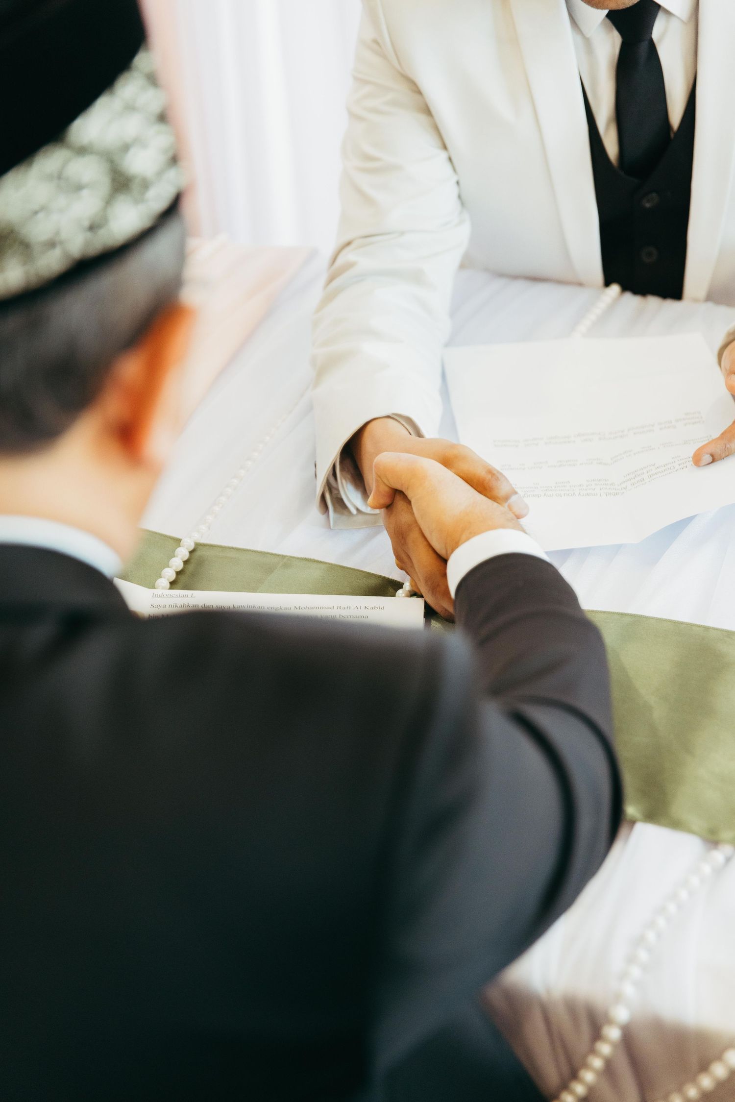 Two men in formal suits shake hands over a table during a Jewish wedding ceremony.